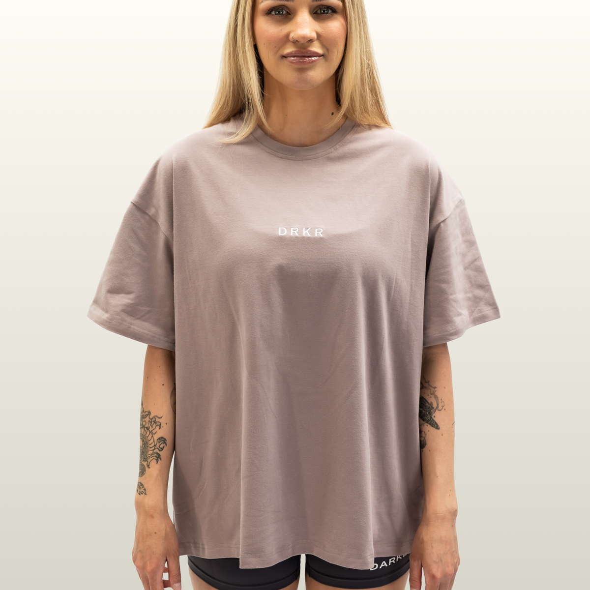 Woman wearing the Endure Oversized Tee in dusty pink with DRKR chest logo, front view