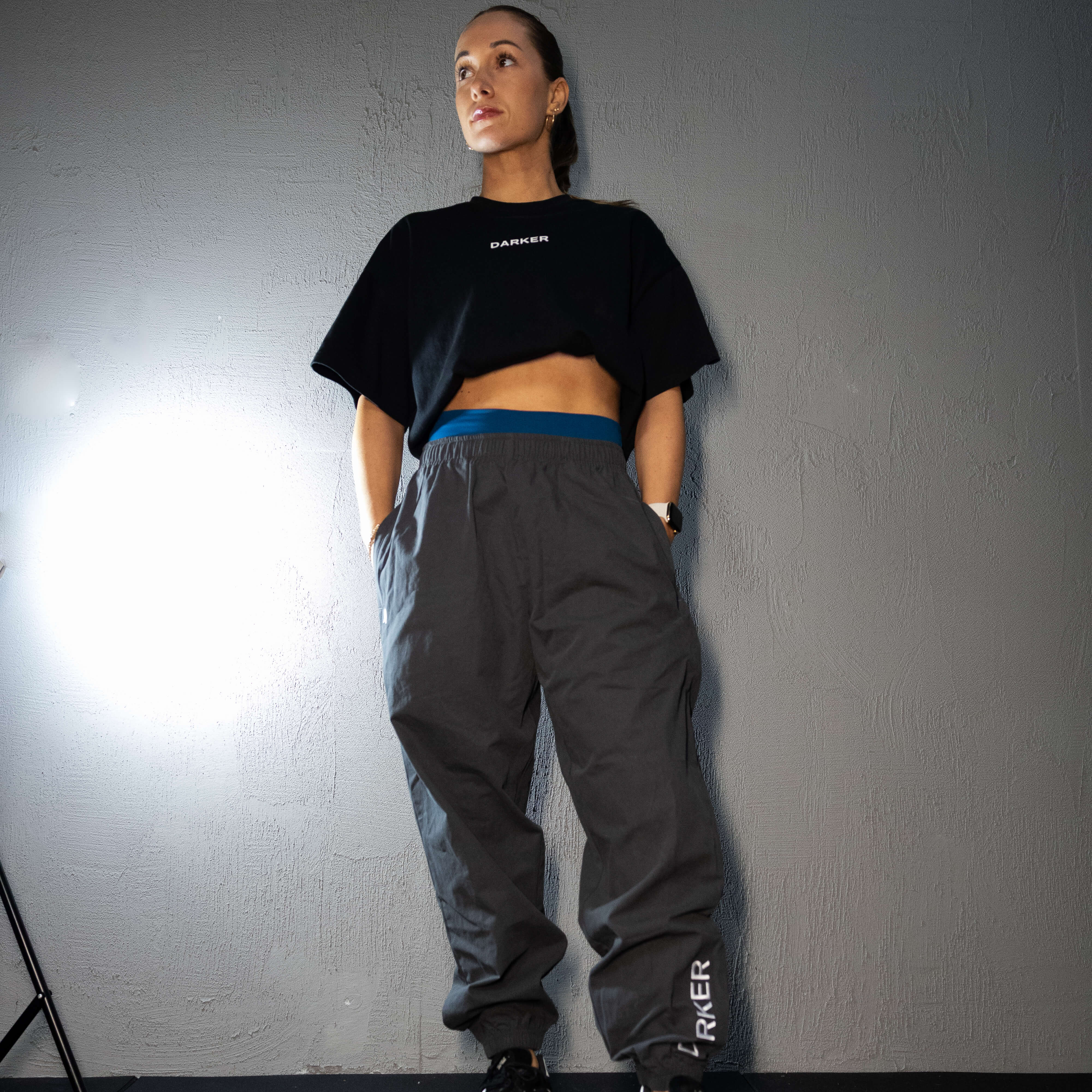 Person wearing a black crop top and gray pants with 'DARKER' branding against a gray wall.