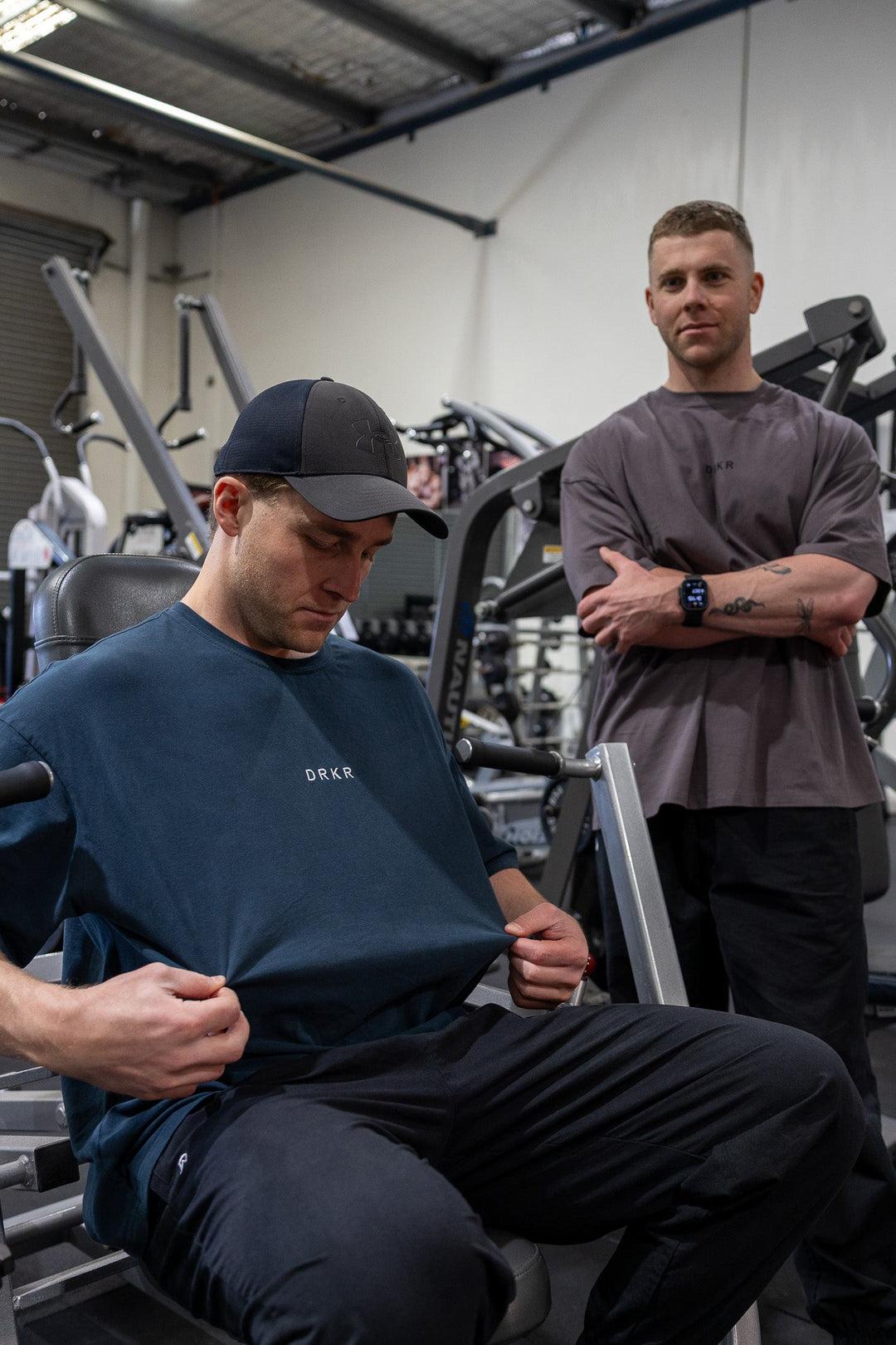 Two men in the gym wearing the Endure Oversized Tee in forest green and storm grey