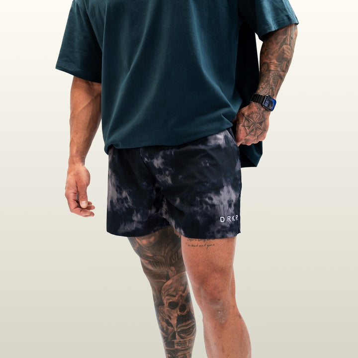 Man wearing the midnight camo Endure 5 inch Shorts with a forest green tee, hand in pocket