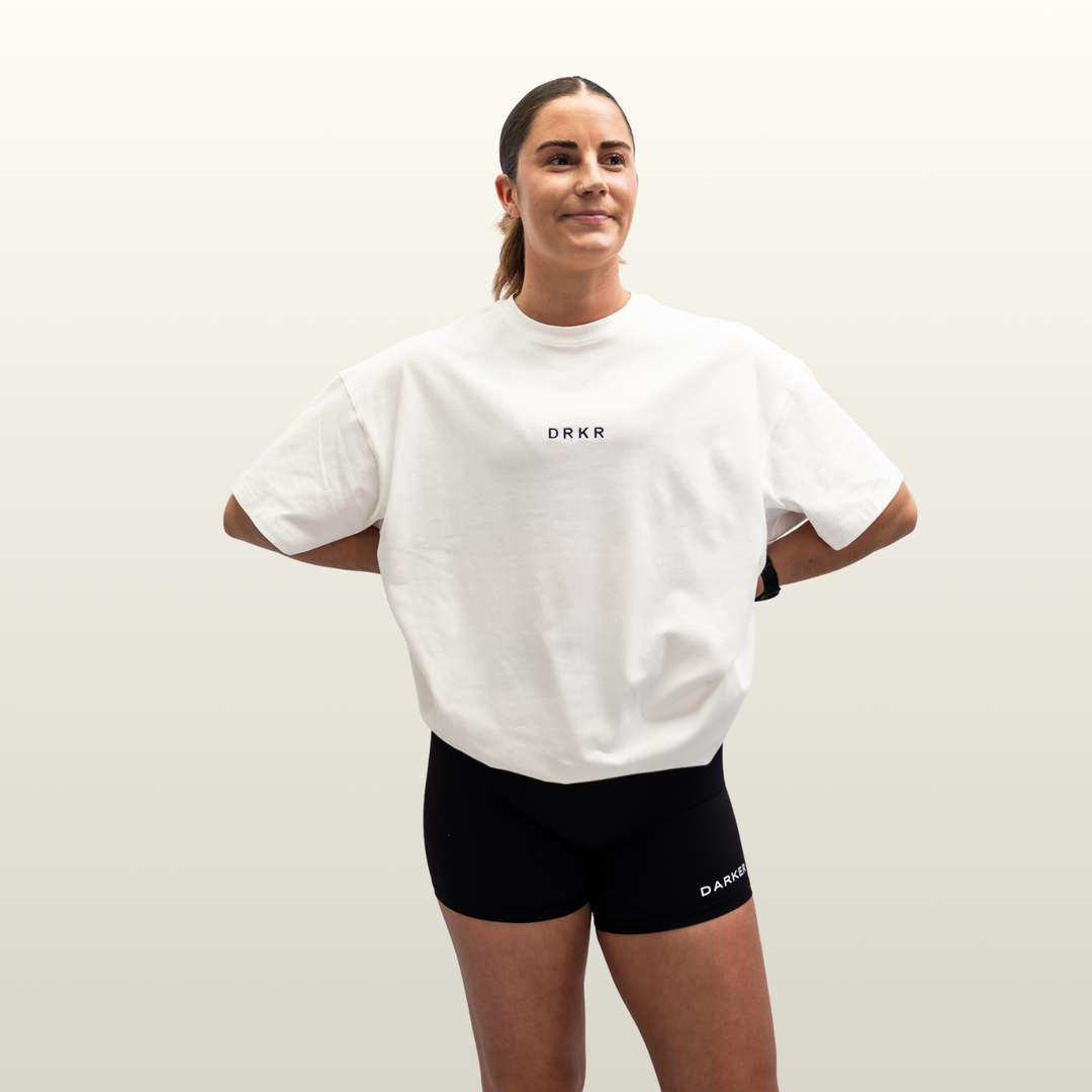 Woman wearing the white Endure Oversized Tee with black shorts, hands on hips