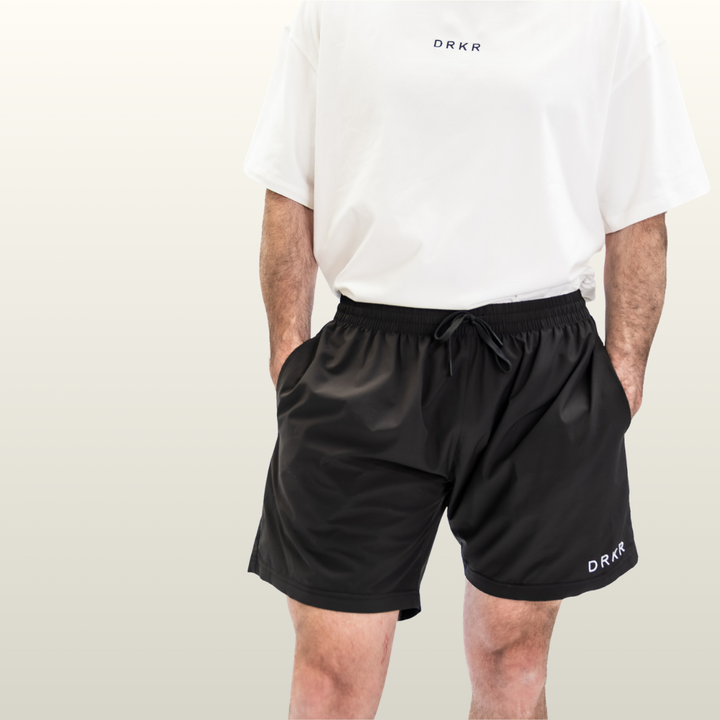 Man wearing the black Endure 7 inch Shorts with a white Endure tee, hands in pockets