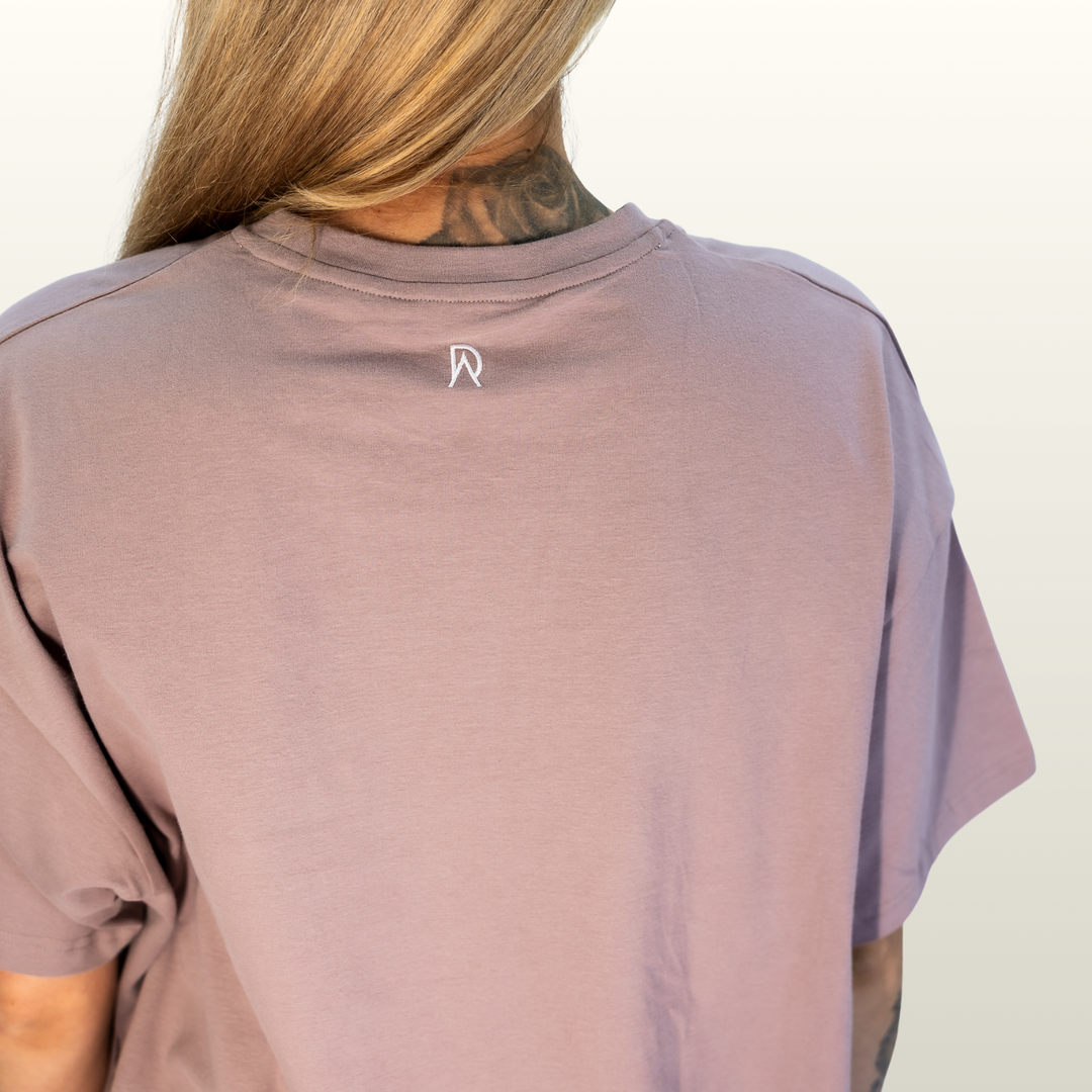 Close-up of the DA monogram on the back neck of the dusty pink Endure Oversized Tee