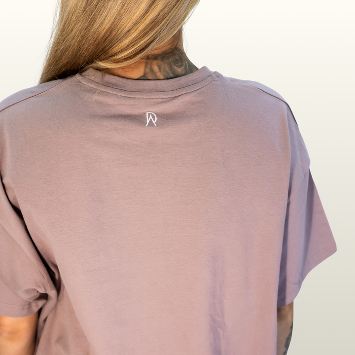 Close-up of the DA monogram on the back neck of the dusty pink Endure Oversized Tee