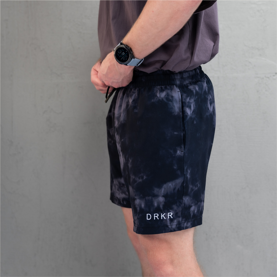 Man wearing the midnight camo Endure 7 inch Shorts against a concrete wall, side view