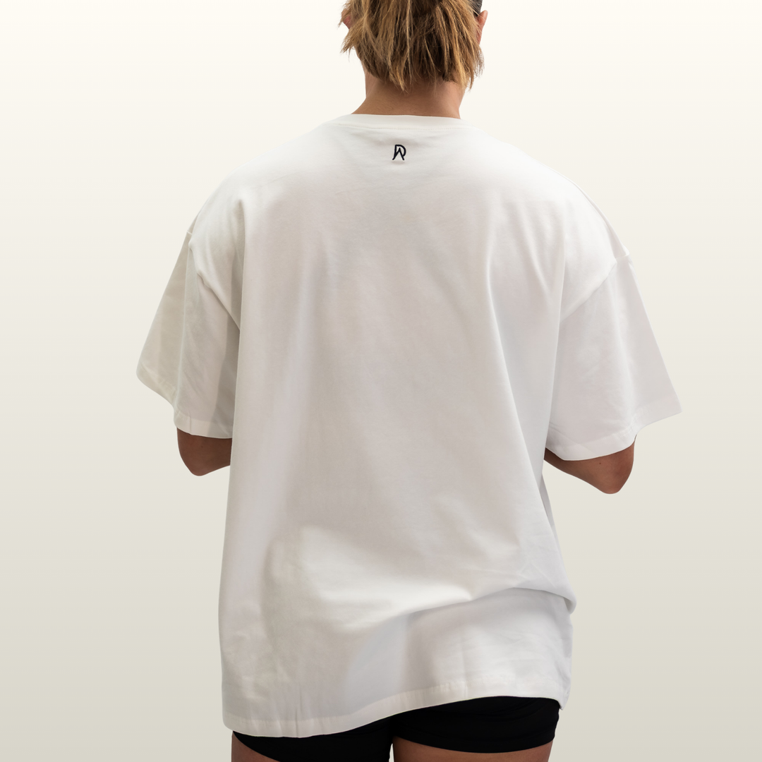 Woman wearing the white Endure Oversized Tee, back view showing the DA monogram