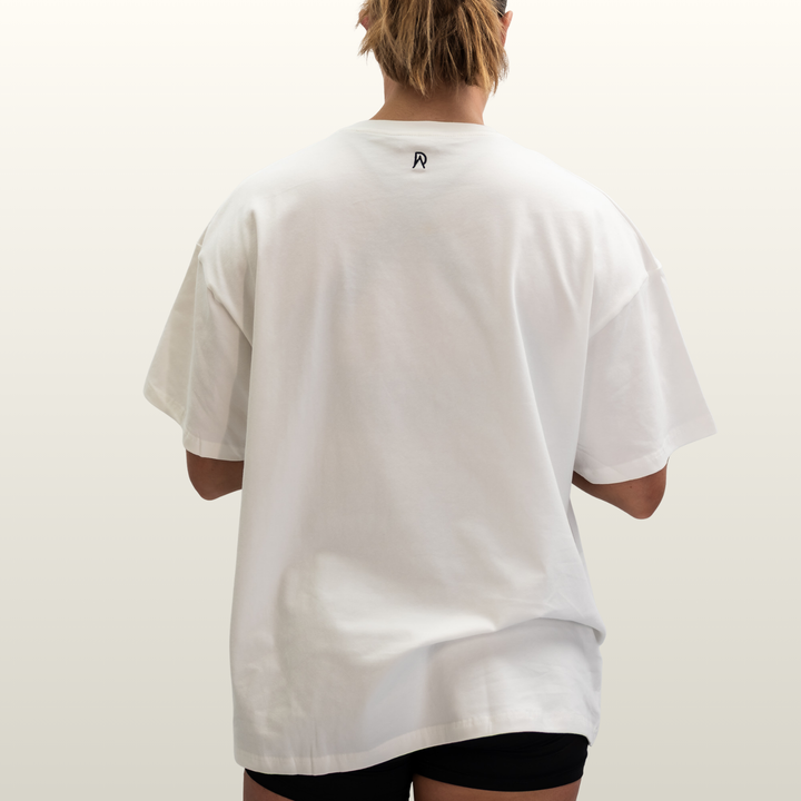 Woman wearing the white Endure Oversized Tee, back view showing the DA monogram