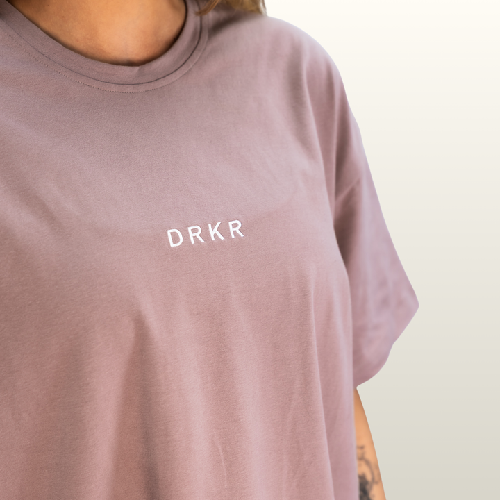 Close-up of the DRKR chest logo on the dusty pink Endure Oversized Tee