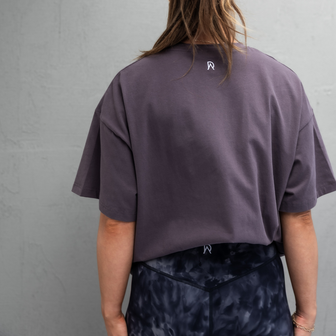 Woman wearing the storm grey Endure Oversized Tee, back view showing the DA monogram