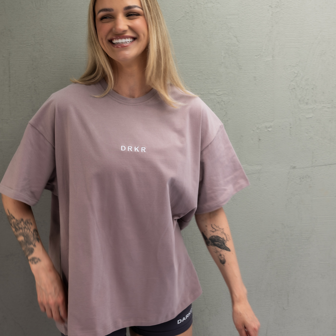 Smiling woman wearing the dusty pink Endure Oversized Tee against a concrete wall