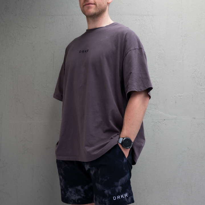 Man wearing the storm grey Endure Oversized Tee with midnight camo Endure Shorts, hand in pocket