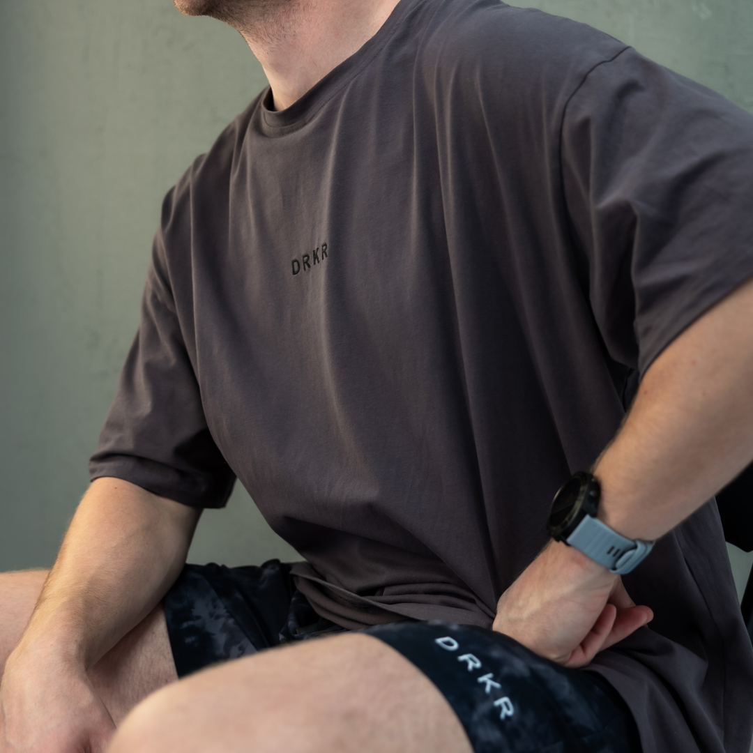 Seated man wearing the storm grey Endure Oversized Tee and midnight camo Endure Shorts