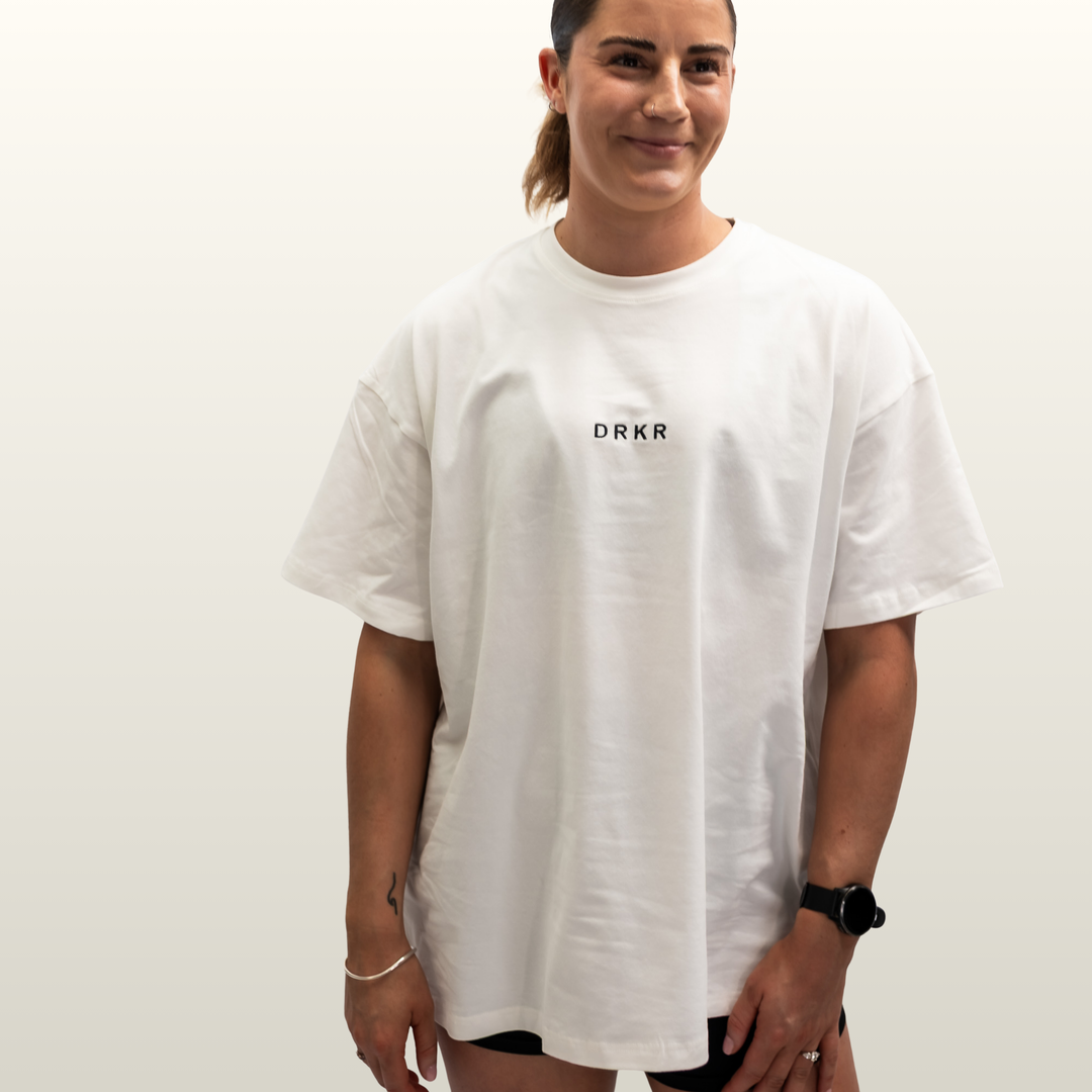 Smiling woman wearing the Endure Oversized Tee in white with DRKR chest logo, front view