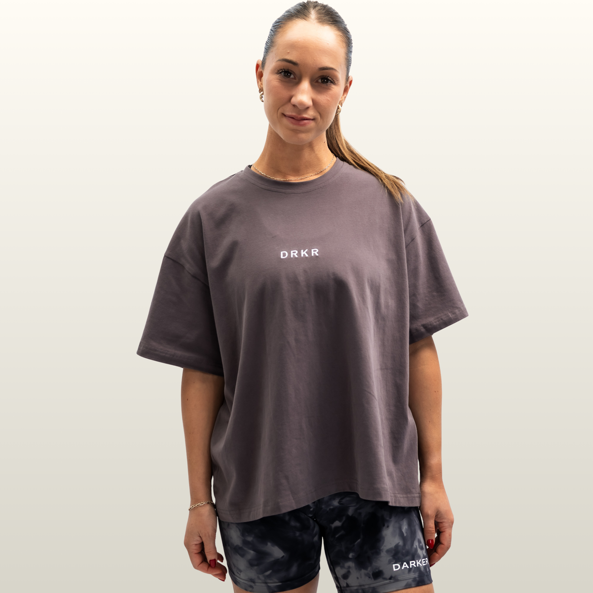 Woman wearing the Endure Oversized Tee in storm grey with DRKR chest logo, front view