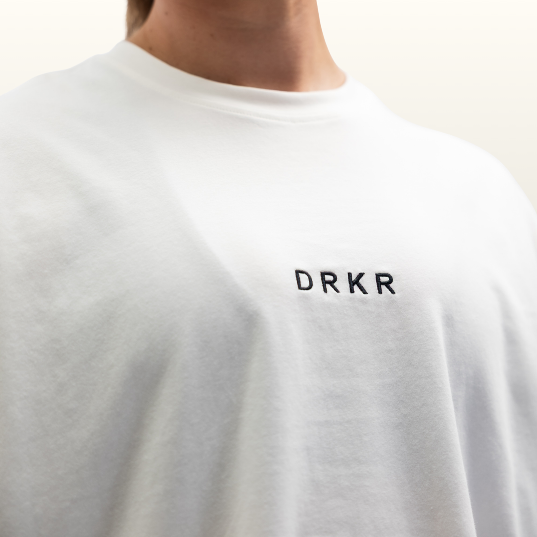 Close-up of the DRKR chest logo on the white Endure Oversized Tee