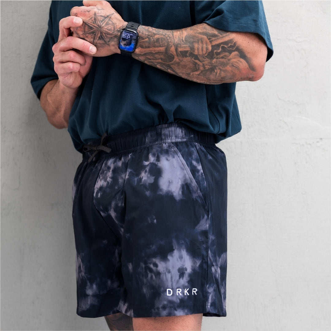 Man wearing the midnight camo Endure 5 inch Shorts against a concrete wall