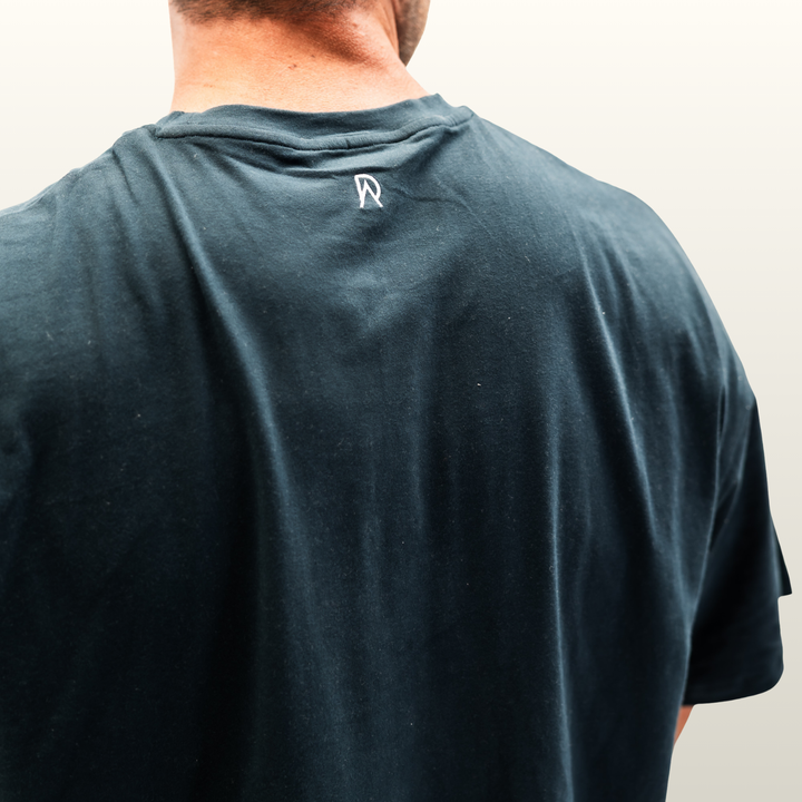 Close-up of the DA monogram on the back neck of the forest green Endure Oversized Tee