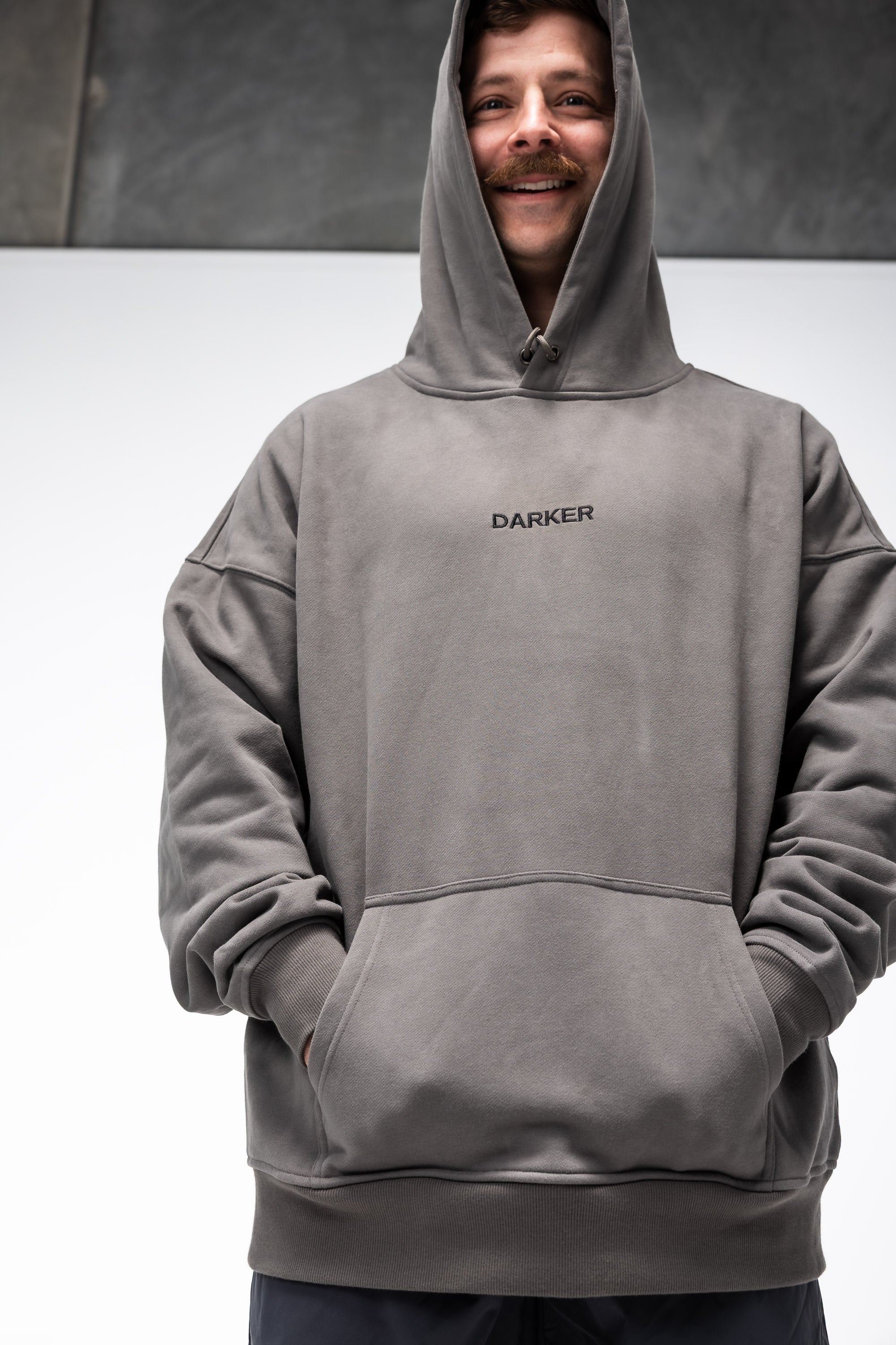 Person wearing a gray hoodie with 'DARKER' branding on a plain background