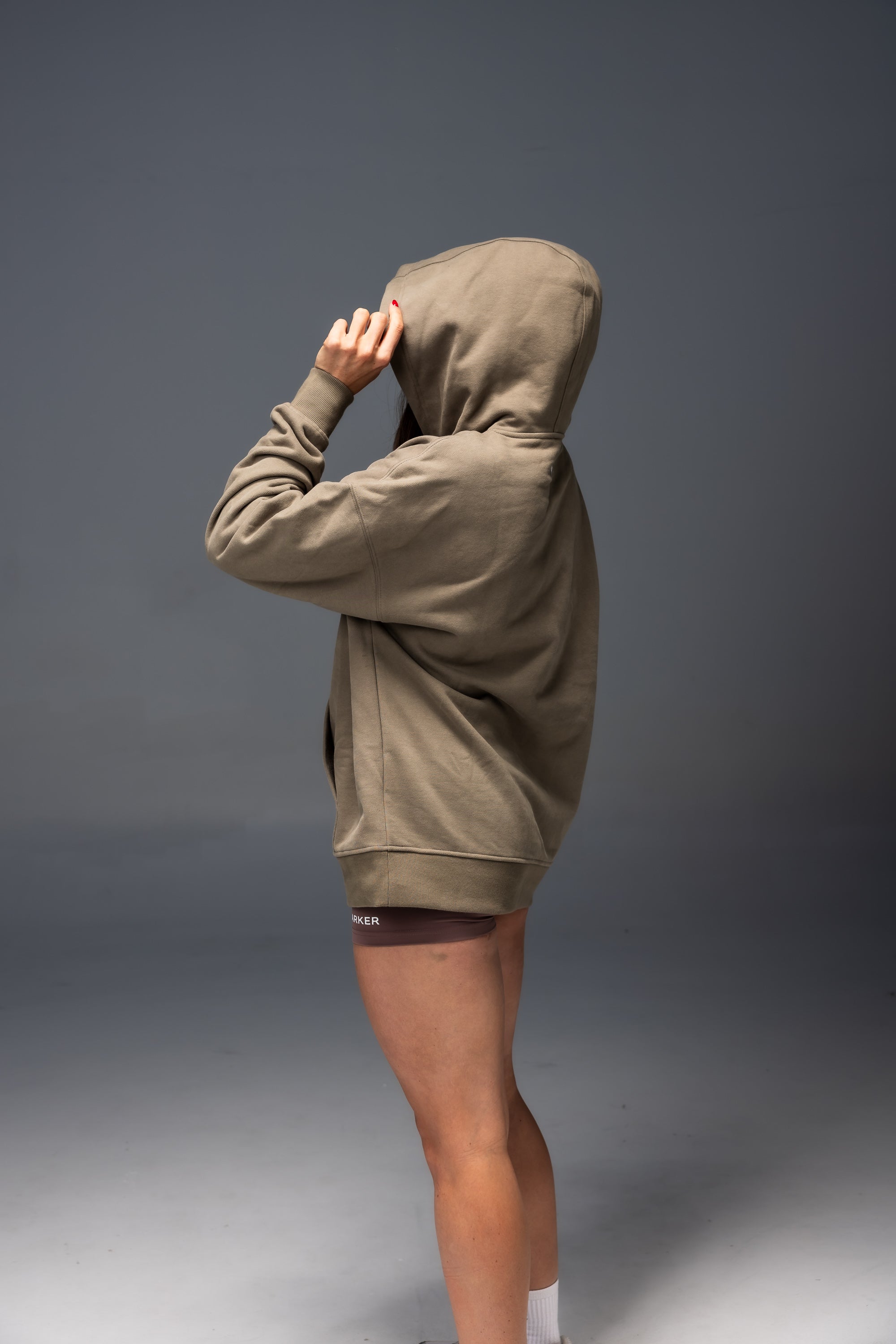 Person wearing a khaki hoodie and shorts on a gray background