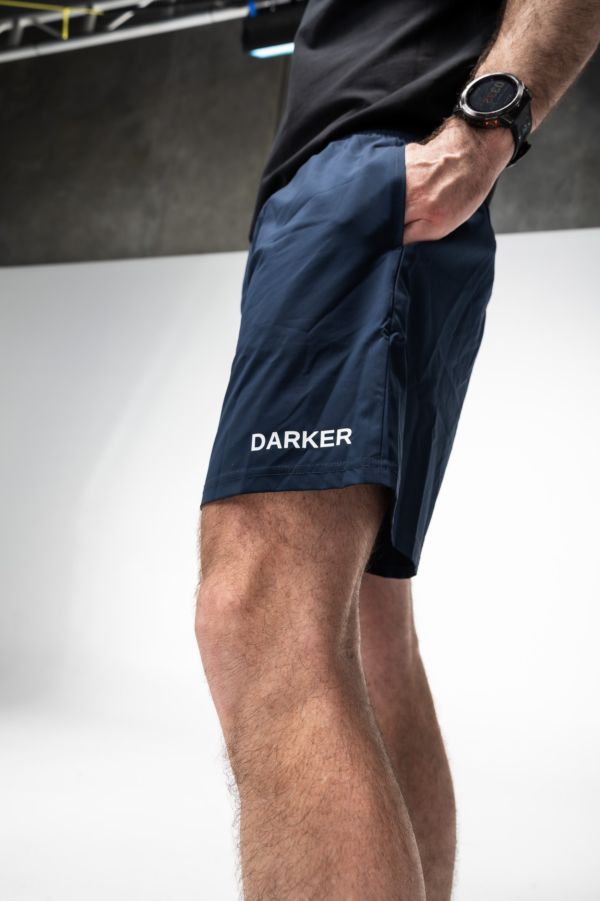 Person wearing navy shorts with 'DARKER' branding on a white background