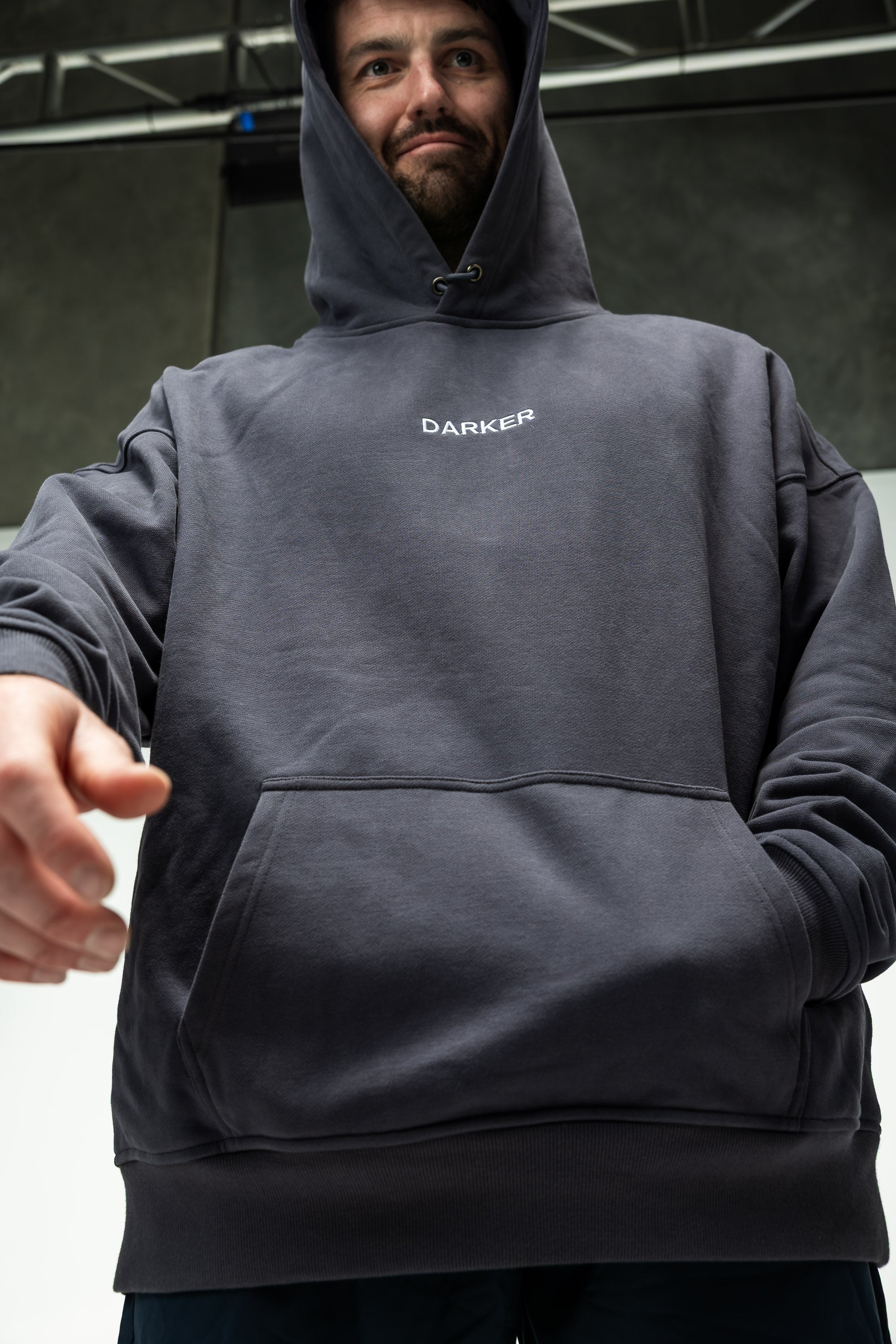 Person wearing a navy hoodie with 'DARKER' branding, pointing forward.