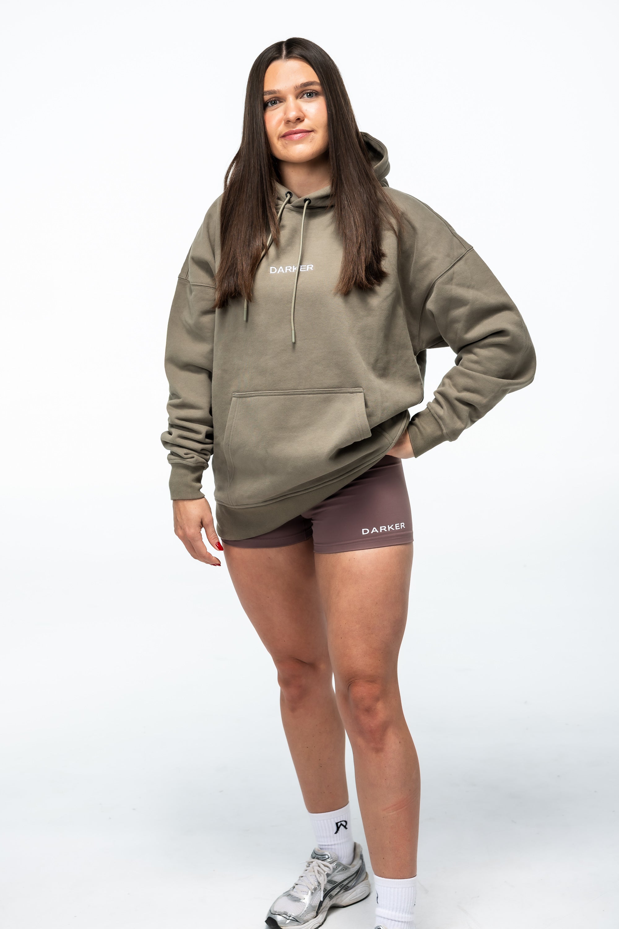 Person wearing a green hoodie and gray shorts on a white background