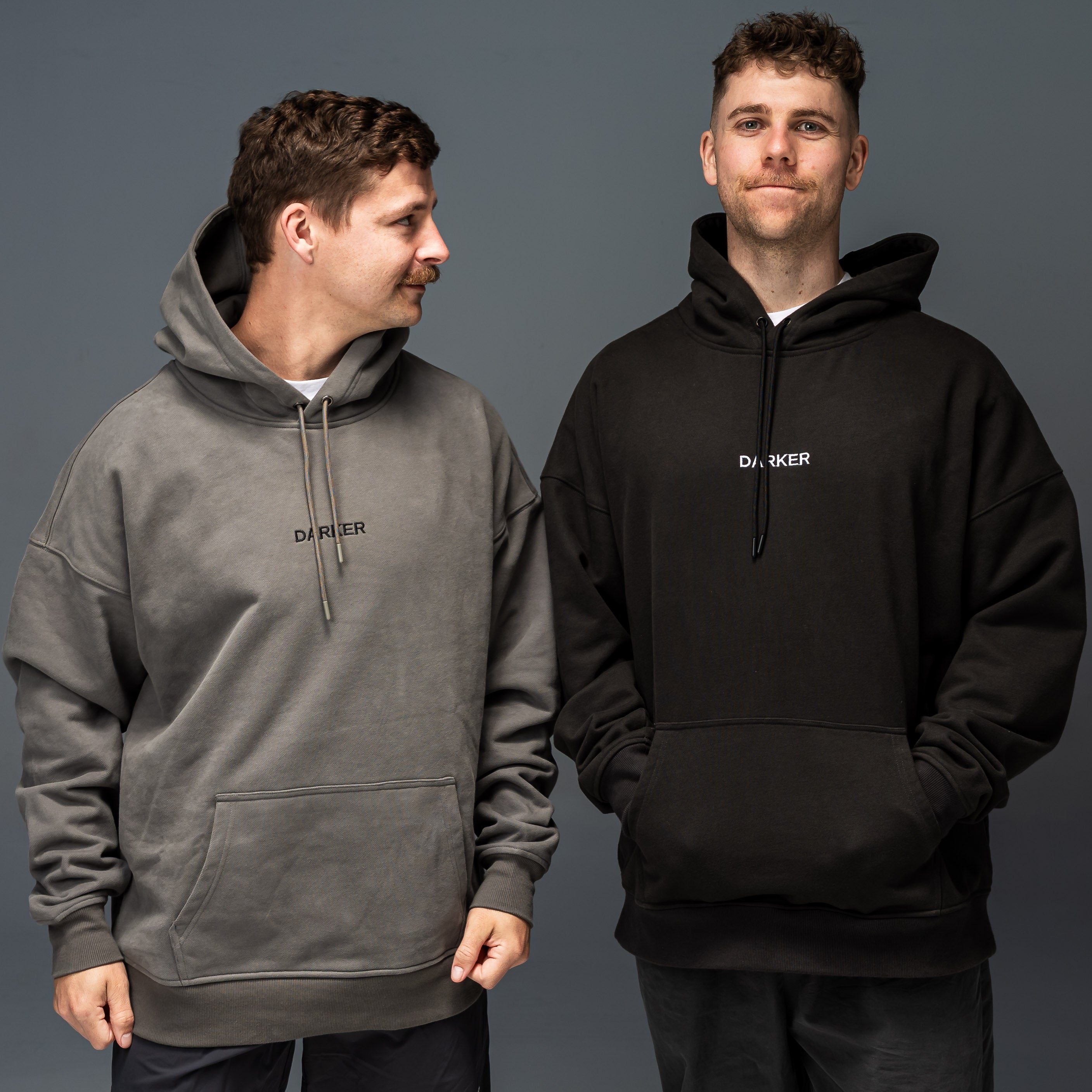 Two men wearing hoodies with 'Darker' branding on a gray background