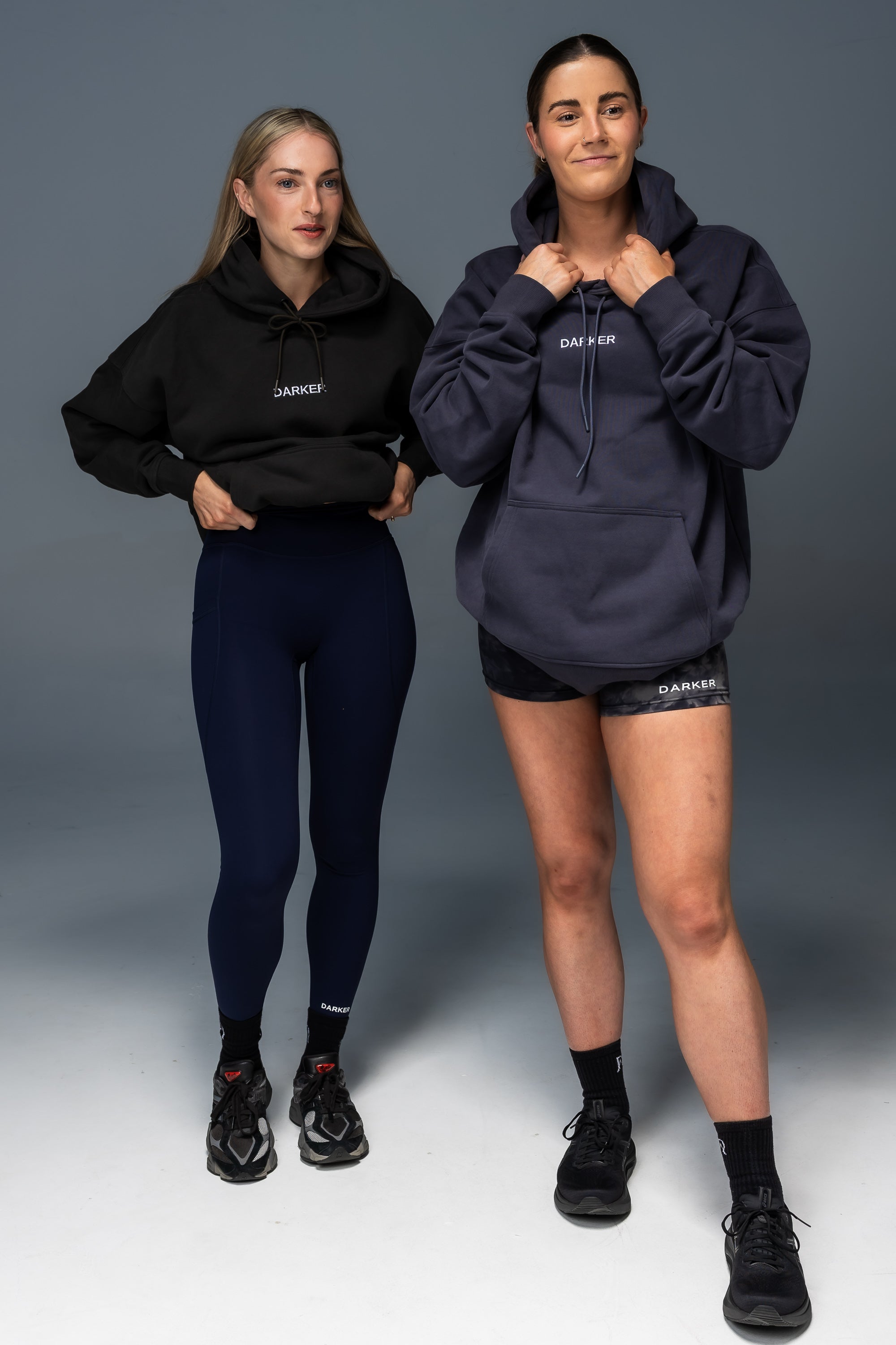 Two women wearing matching black and navy athletic outfits on a gray background