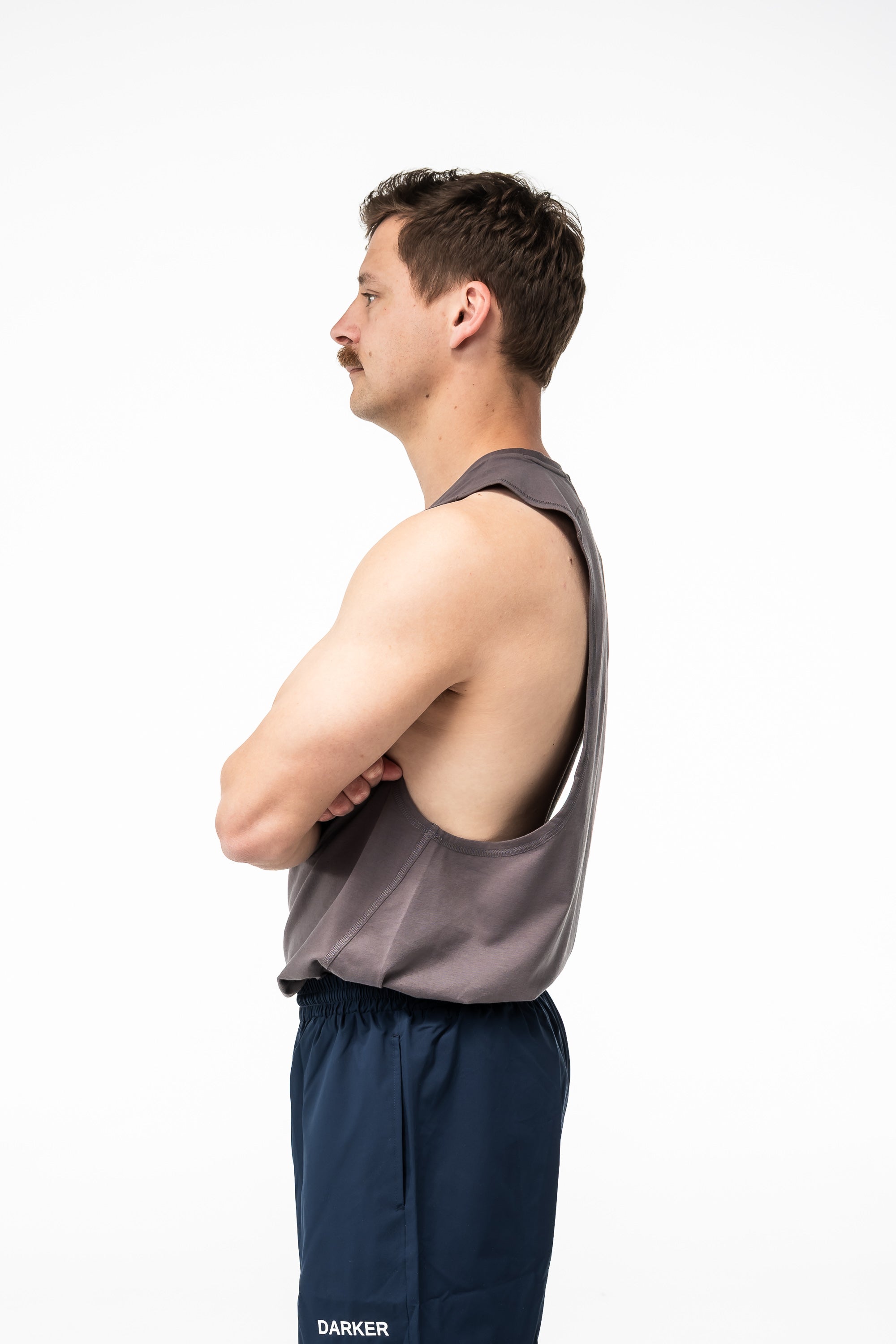Man wearing a gray tank top and navy pants on a white background
