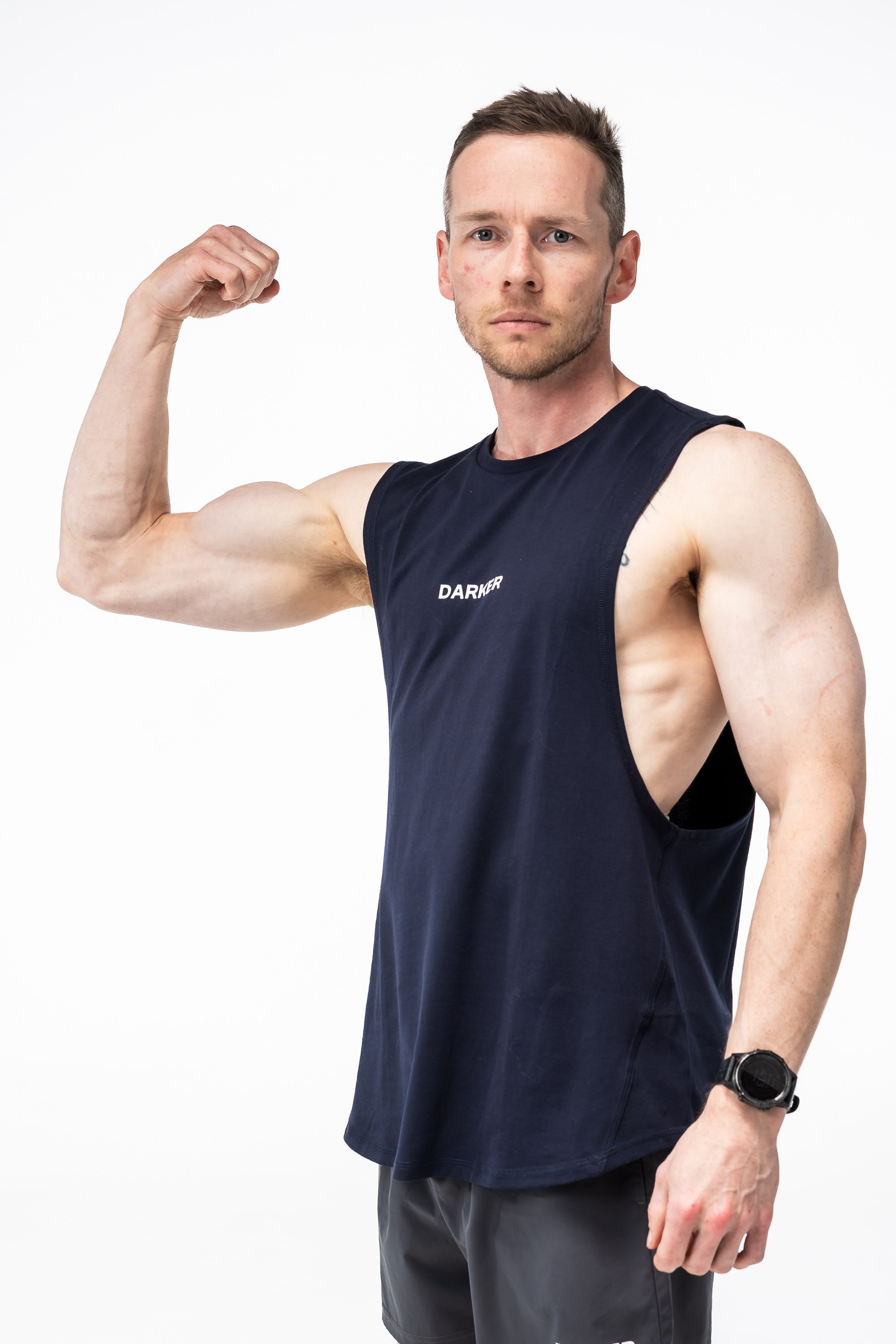 Man flexing his arm wearing a navy tank with a brand logo on a white background