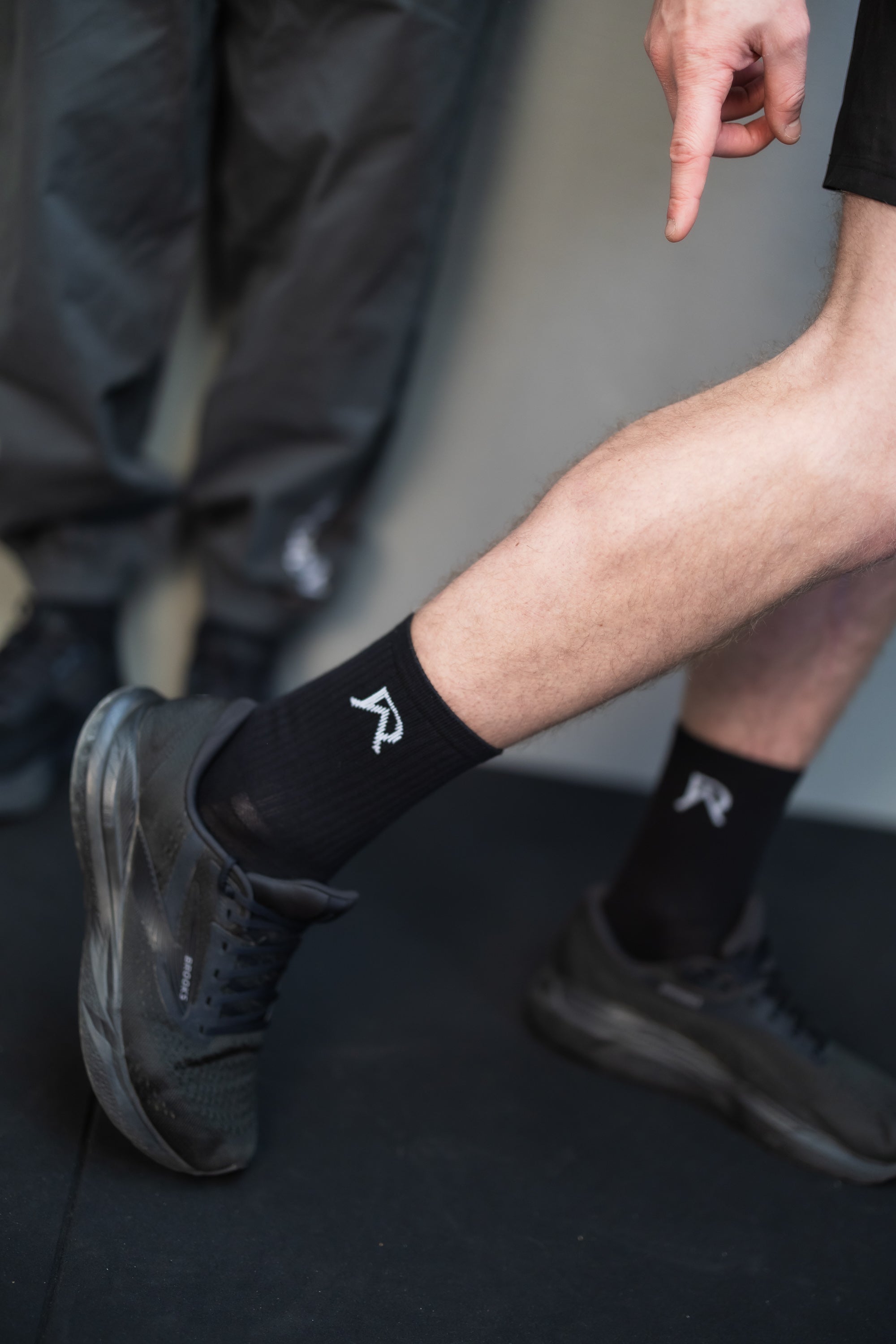 Person wearing black socks with a logo, standing on a dark surface.