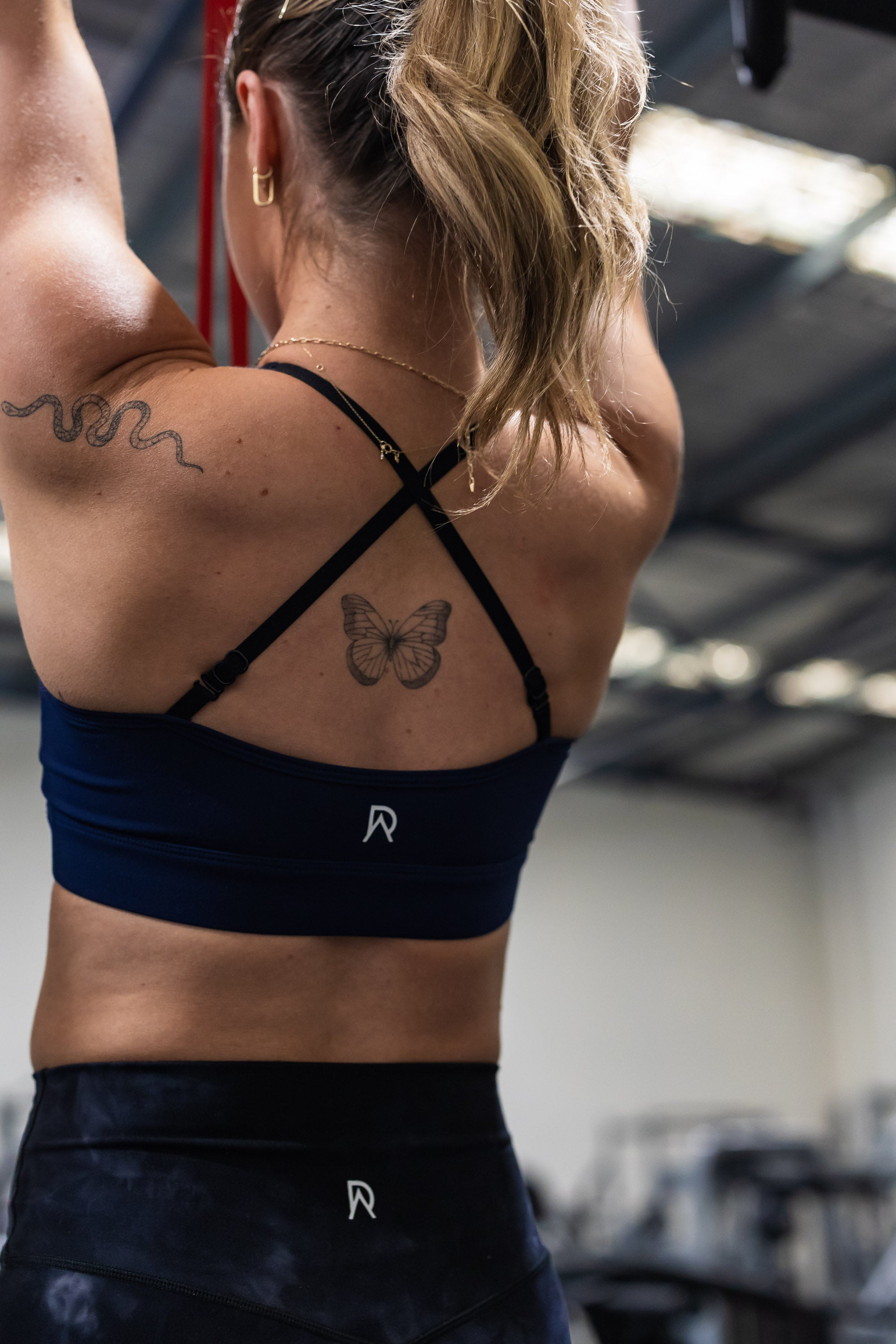 Person wearing a Navy DARKER sports bra with a visible brand logo in an indoor setting doing an assisted pull up