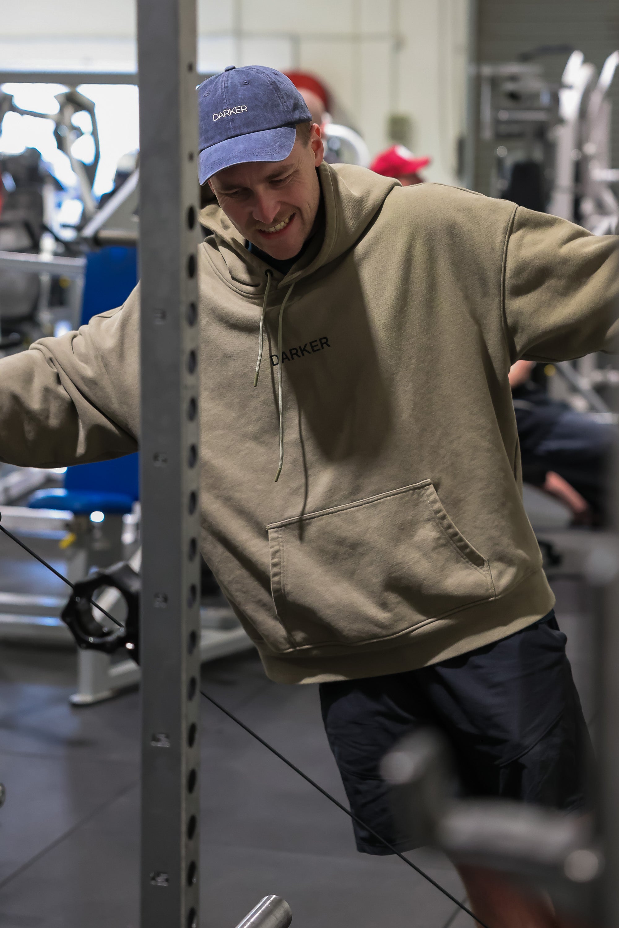 Person wearing a cap and khaki hoodie in a gym setting