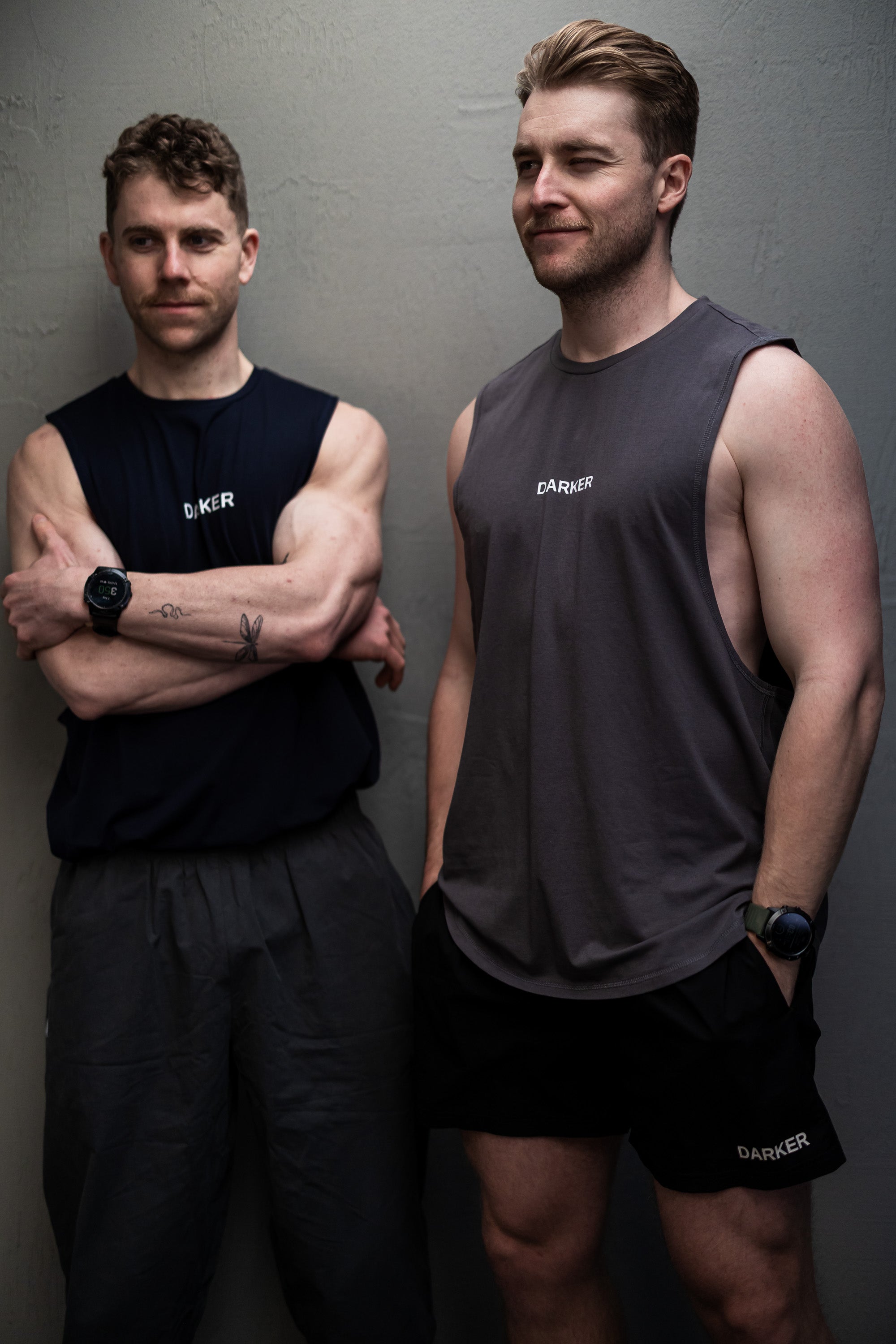 Two men wearing dark athletic grey wear with visible branding against a grey background