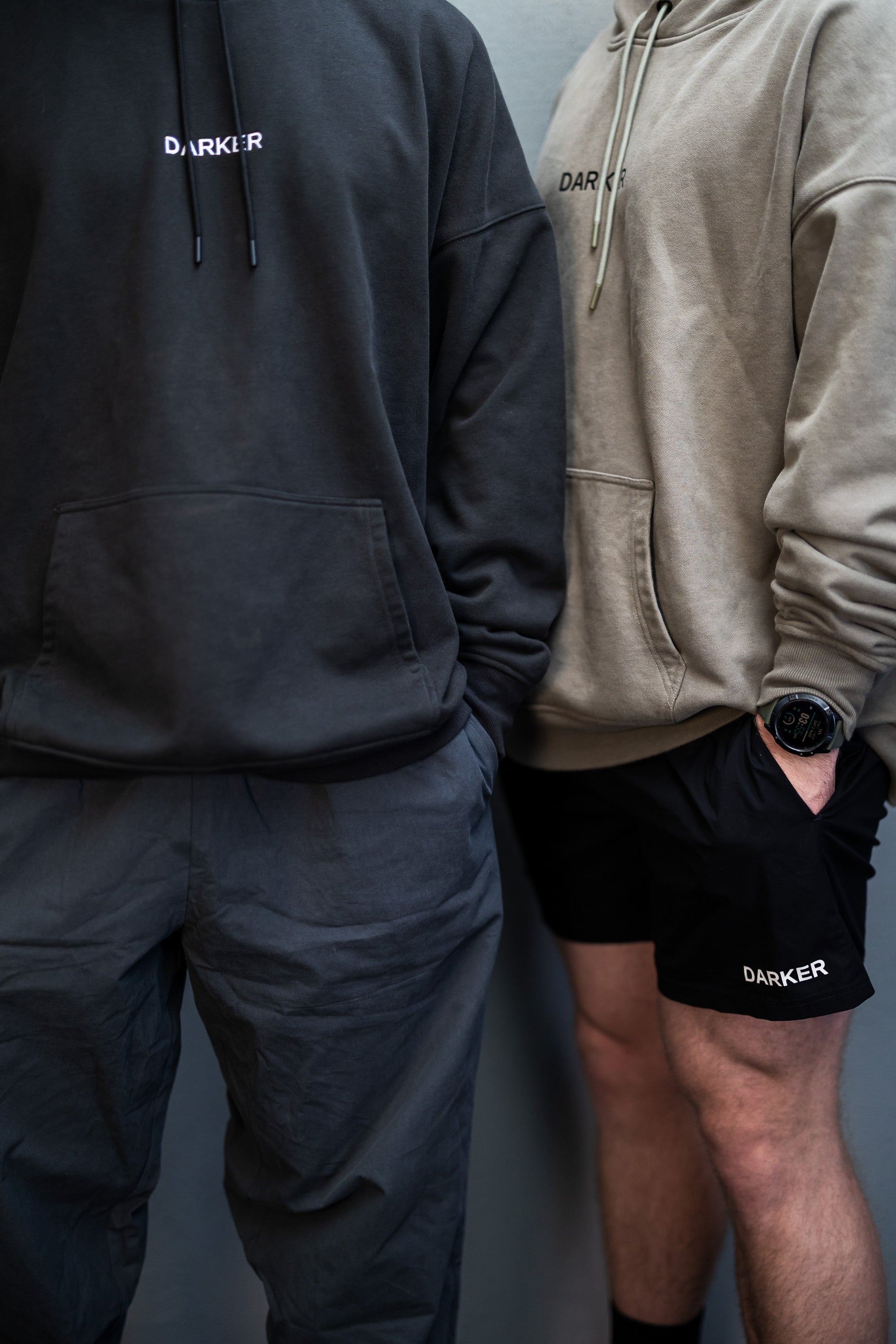 Two people wearing a black and khaki hoodies with 'DARKER' branding, standing against a plain background.