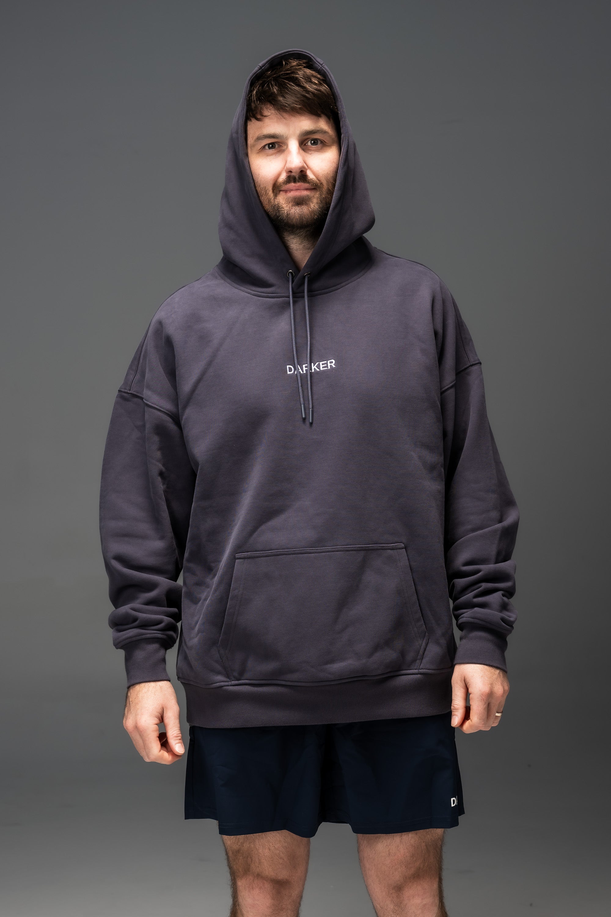 Man wearing a navy hoodie with a brand logo on a gray background