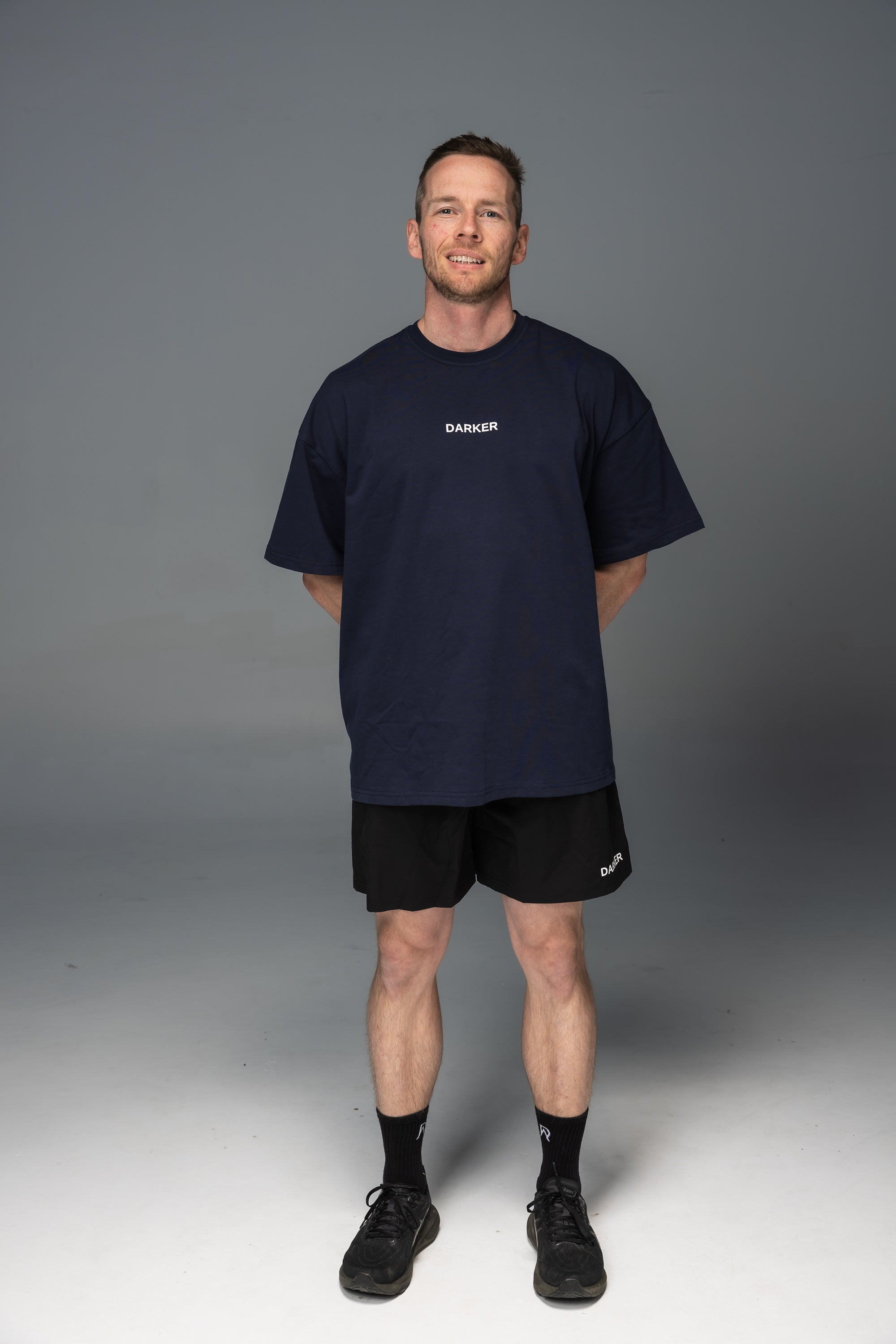Man wearing a navy blue t-shirt and black shorts on a gray background