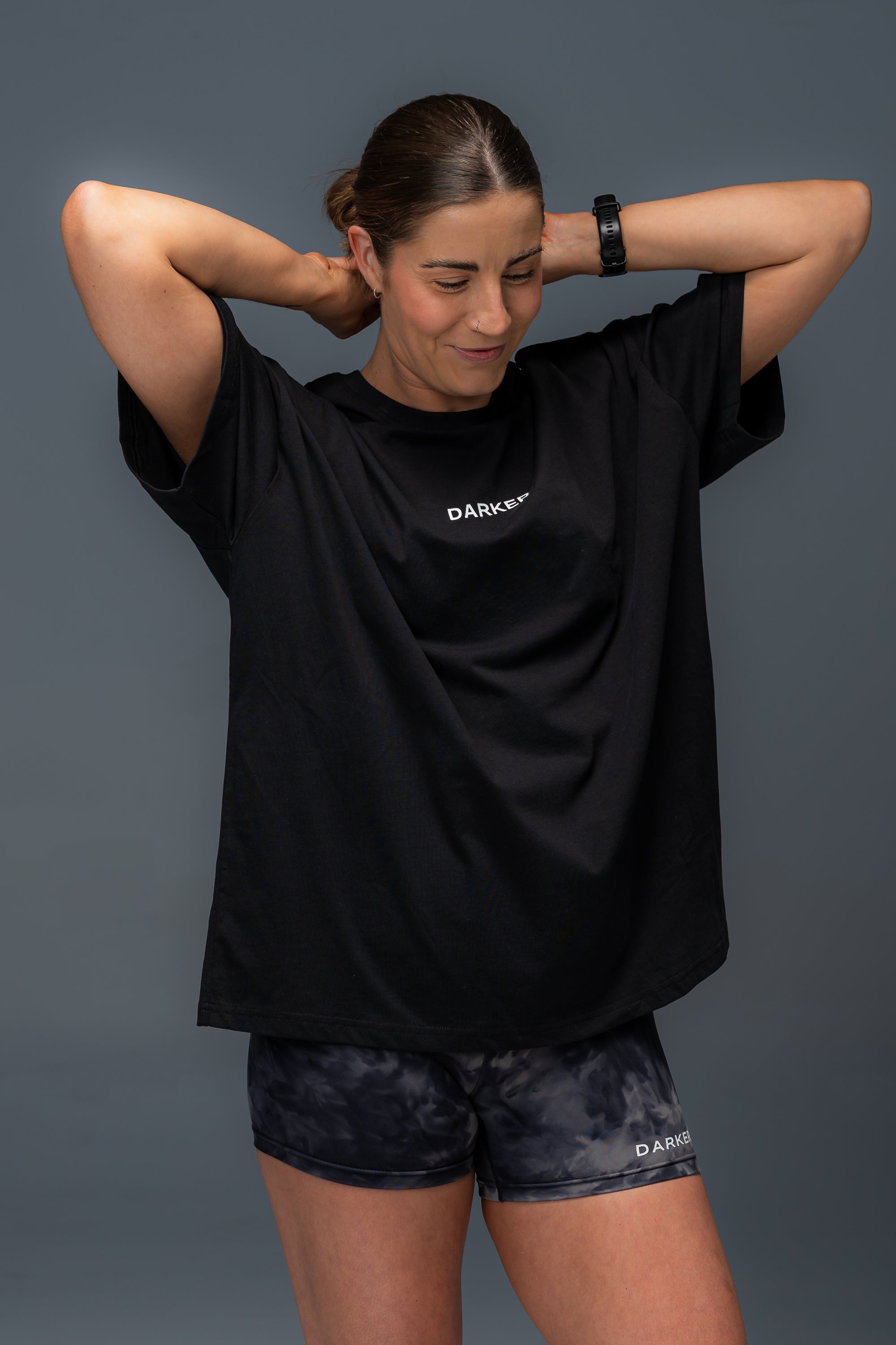 Women wearing a black t-shirt and shorts with a DARKER brand logo, standing against a gray background