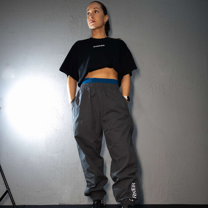 Person wearing a black crop top and gray pants with 'DARKER' branding against a gray wall.