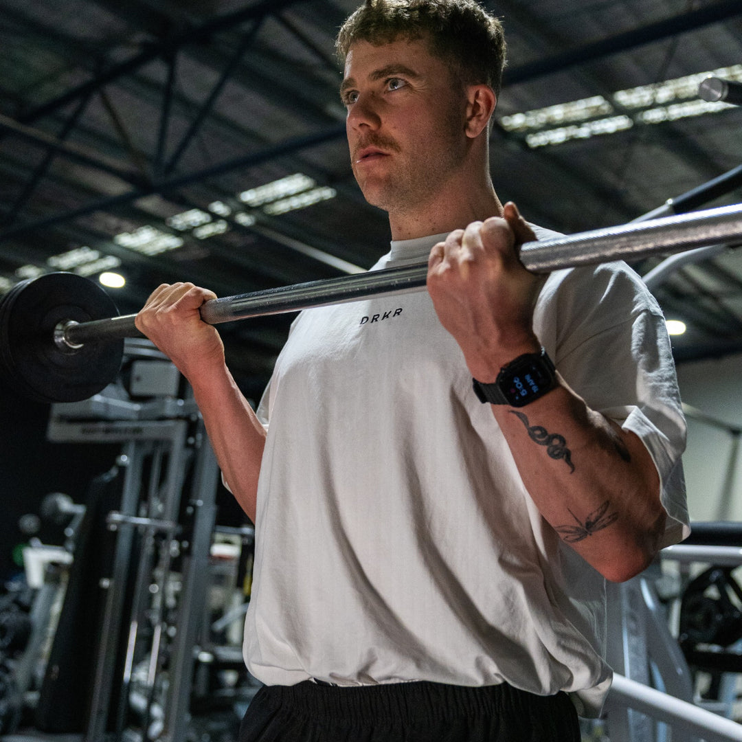 Man doing barbell curls in the gym wearing the white Endure Oversized Tee