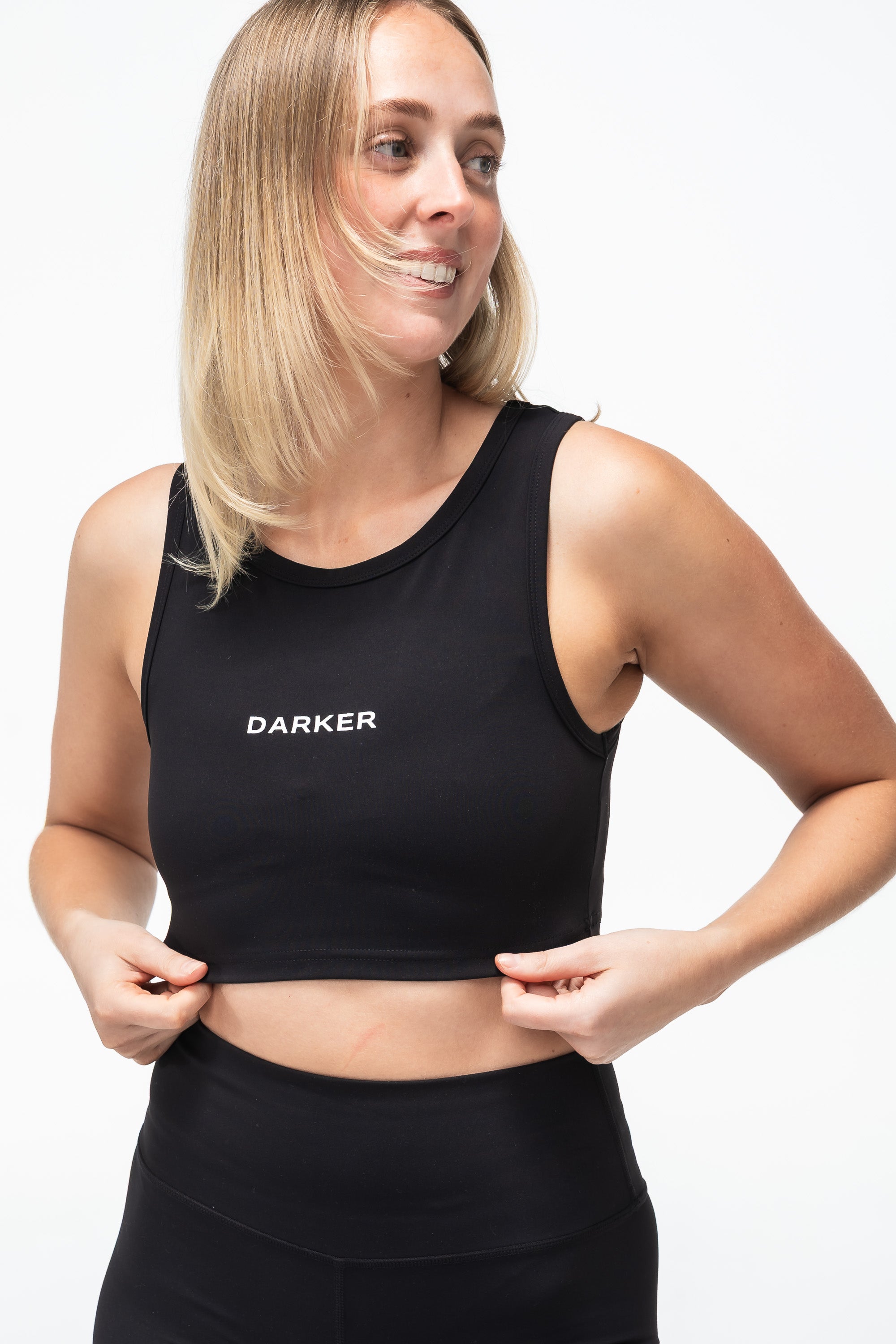 Woman wearing a black cropped tank with 'DARKER' branding on a white background