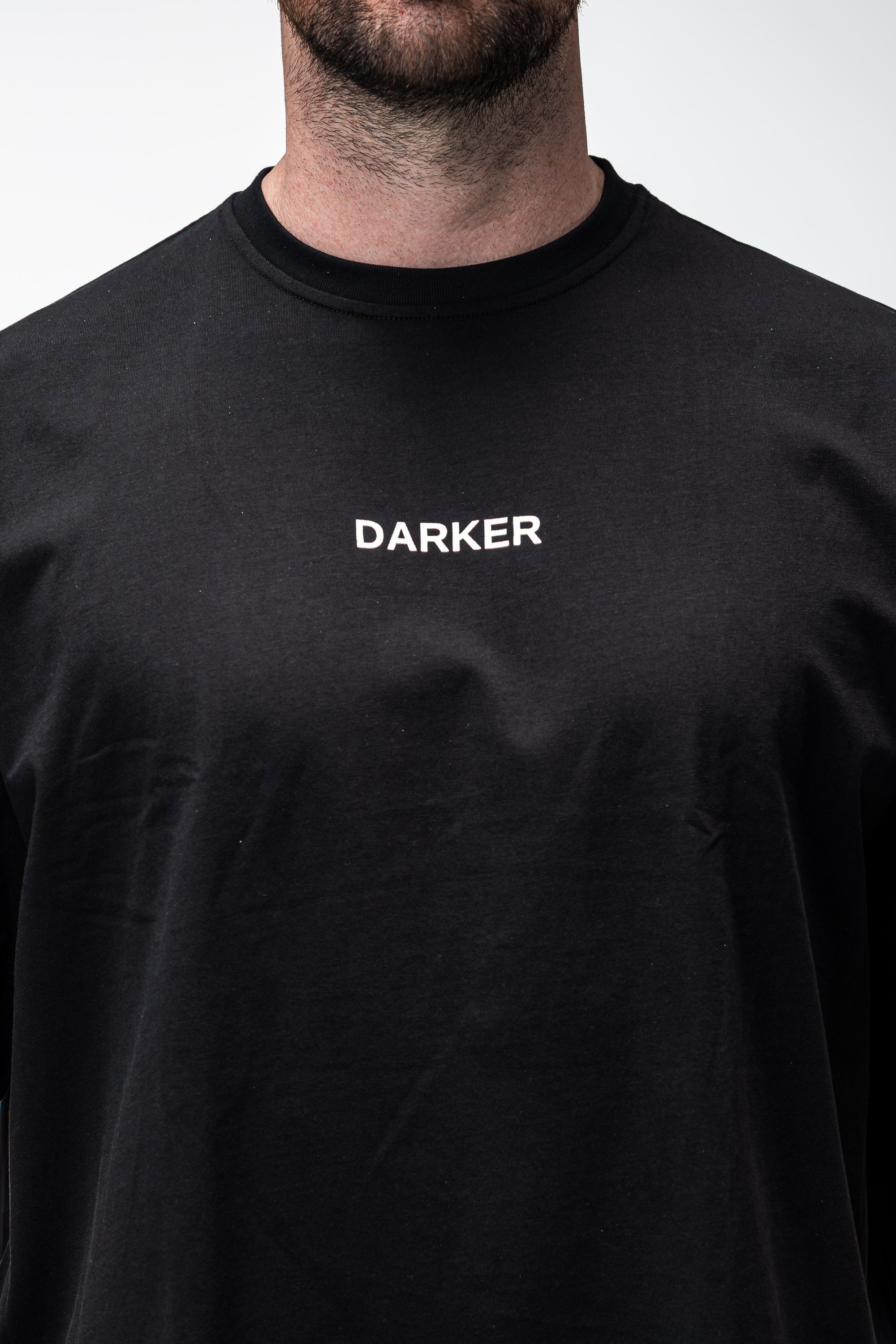 Black t-shirt with 'DARKER' logo worn by a person on a white background