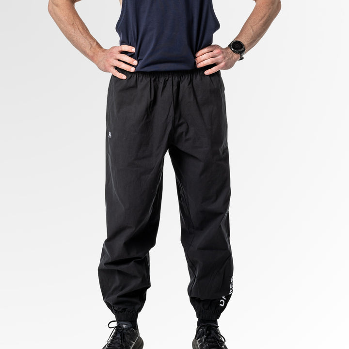 Person wearing black drift pants with DARKER logo on the leg and a navy sleeveless top on a white background