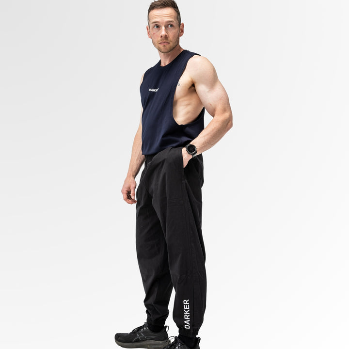 Man wearing a black sleeveless shirt and pants with 'DARKER' branding on a light gray background
