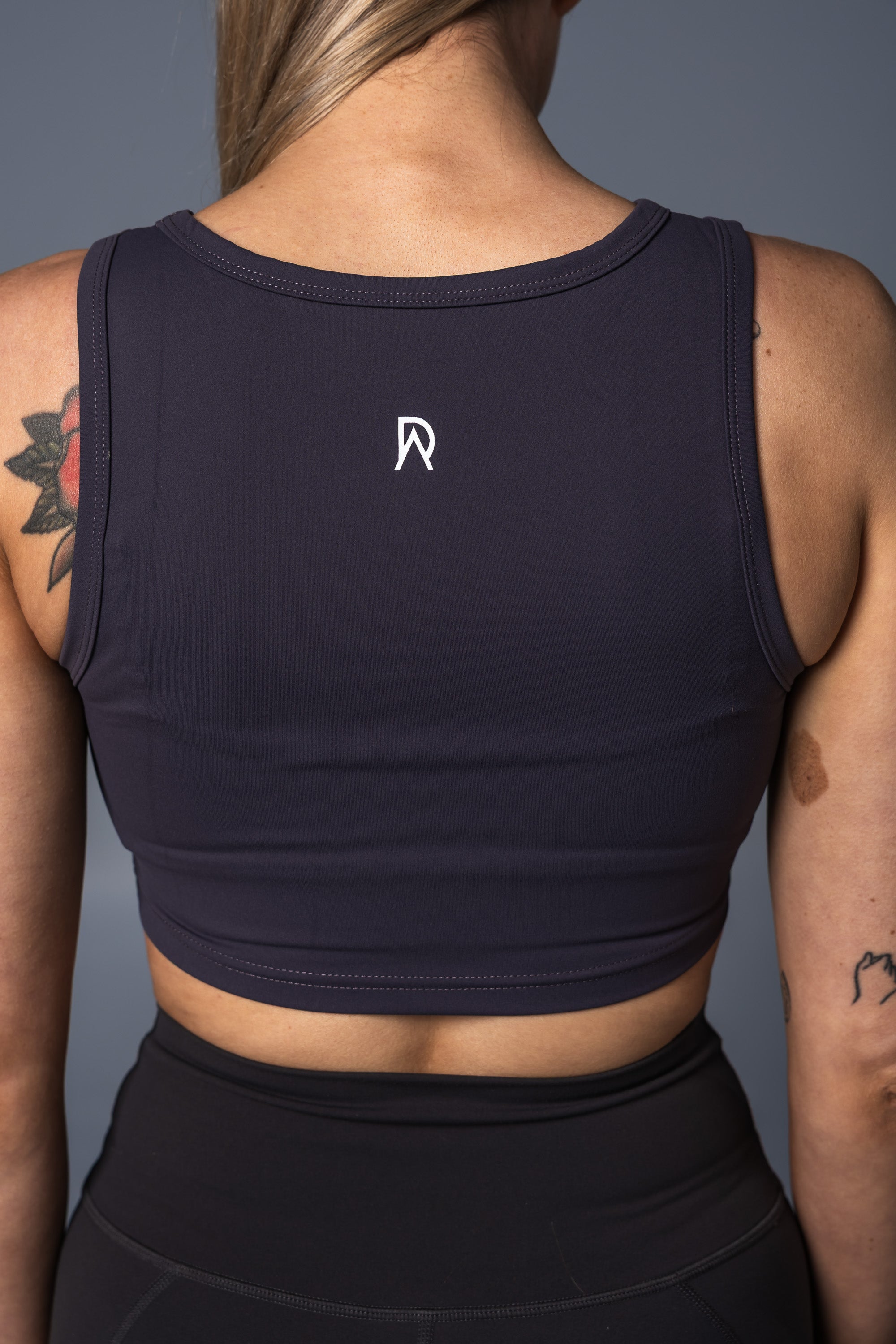 Person wearing a grey cropped tank with a DA logo on a gray background