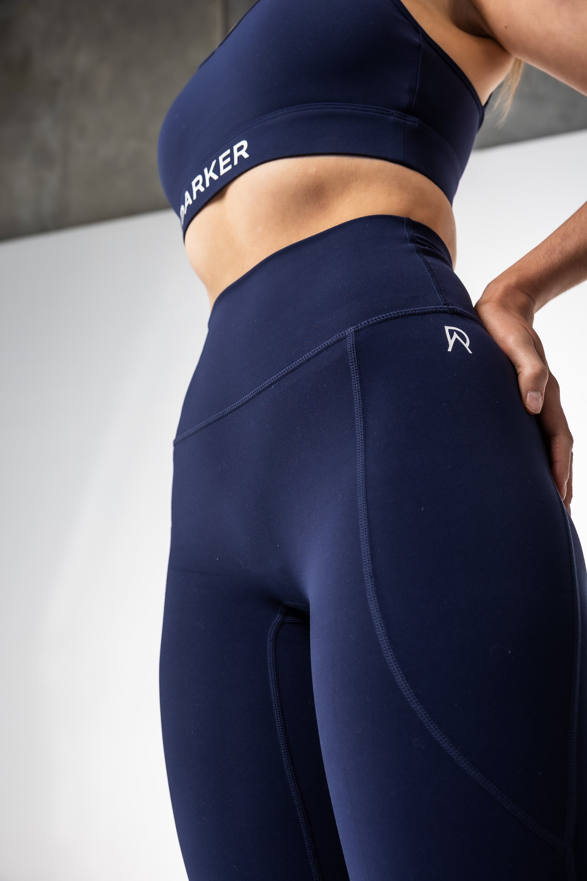 Person wearing navy blue  DARKER athletic leggings with a brand logo on a light background