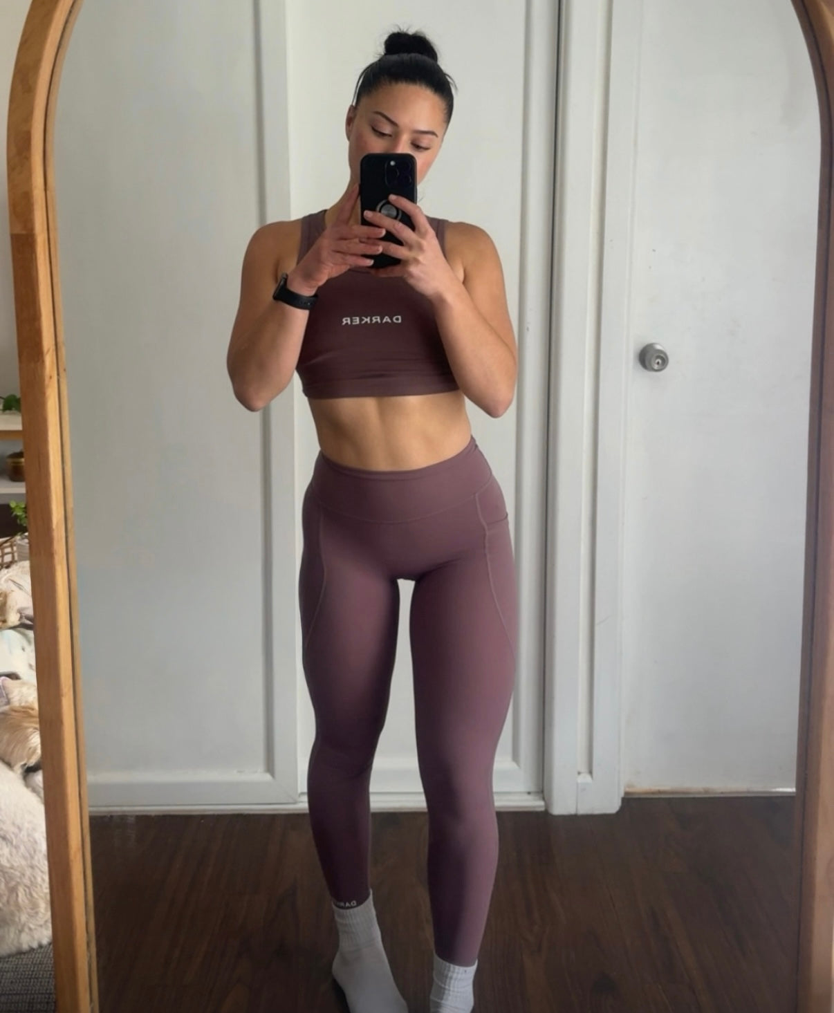 A woman takes a mirror selfie wearing a matching mauve activewear set consisting of a sports bra and high-waisted leggings. The brand name 'DARKER' is printed in white on the sports bra.