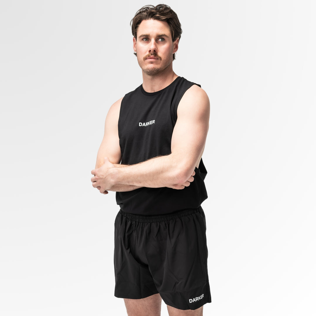 Man wearing a black sleeveless shirt and shorts with 'DARKER' branding on a white background