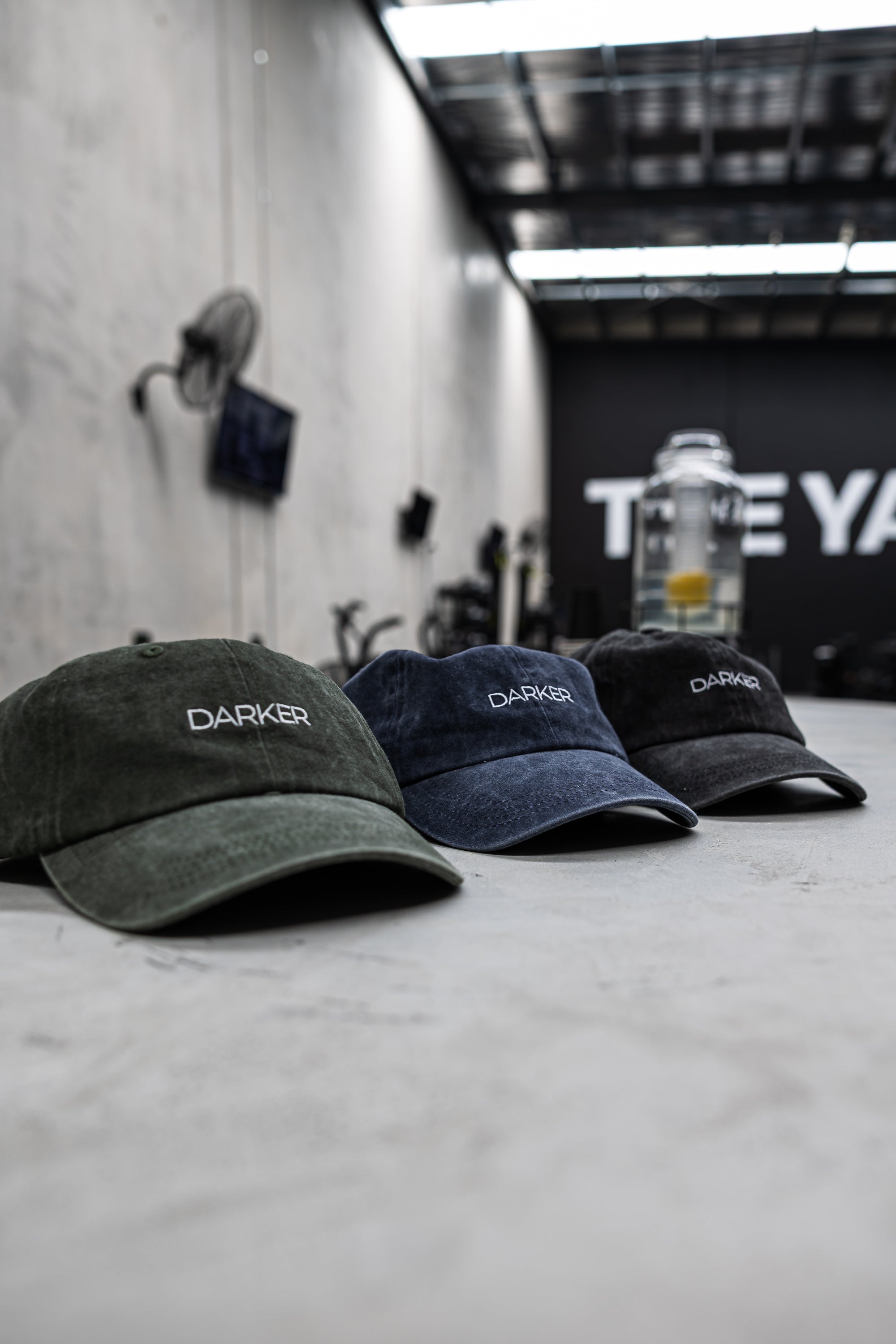 Three caps with 'DARKER' branding on a concrete floor with a blurred background.